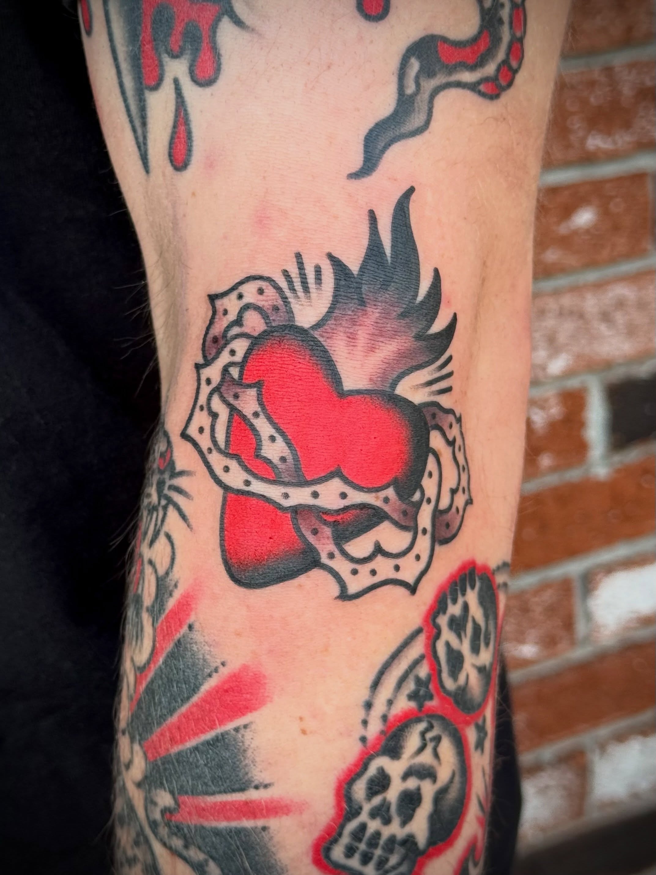 Heart with flames American traditional tattoo on the forearm by Maximilian Harrison