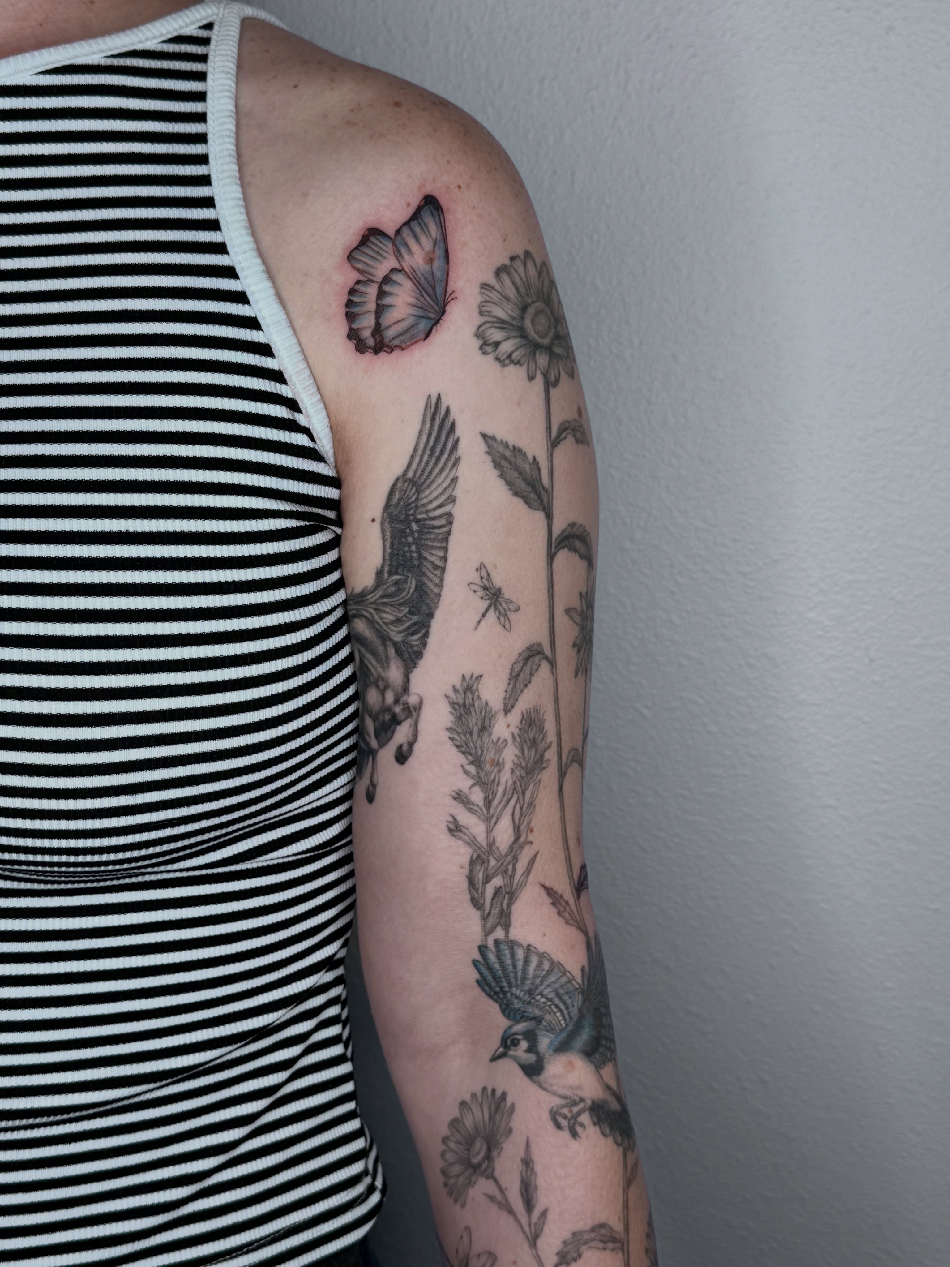 Bird and floral realism tattoo on the upper arm by Ashley Limon
