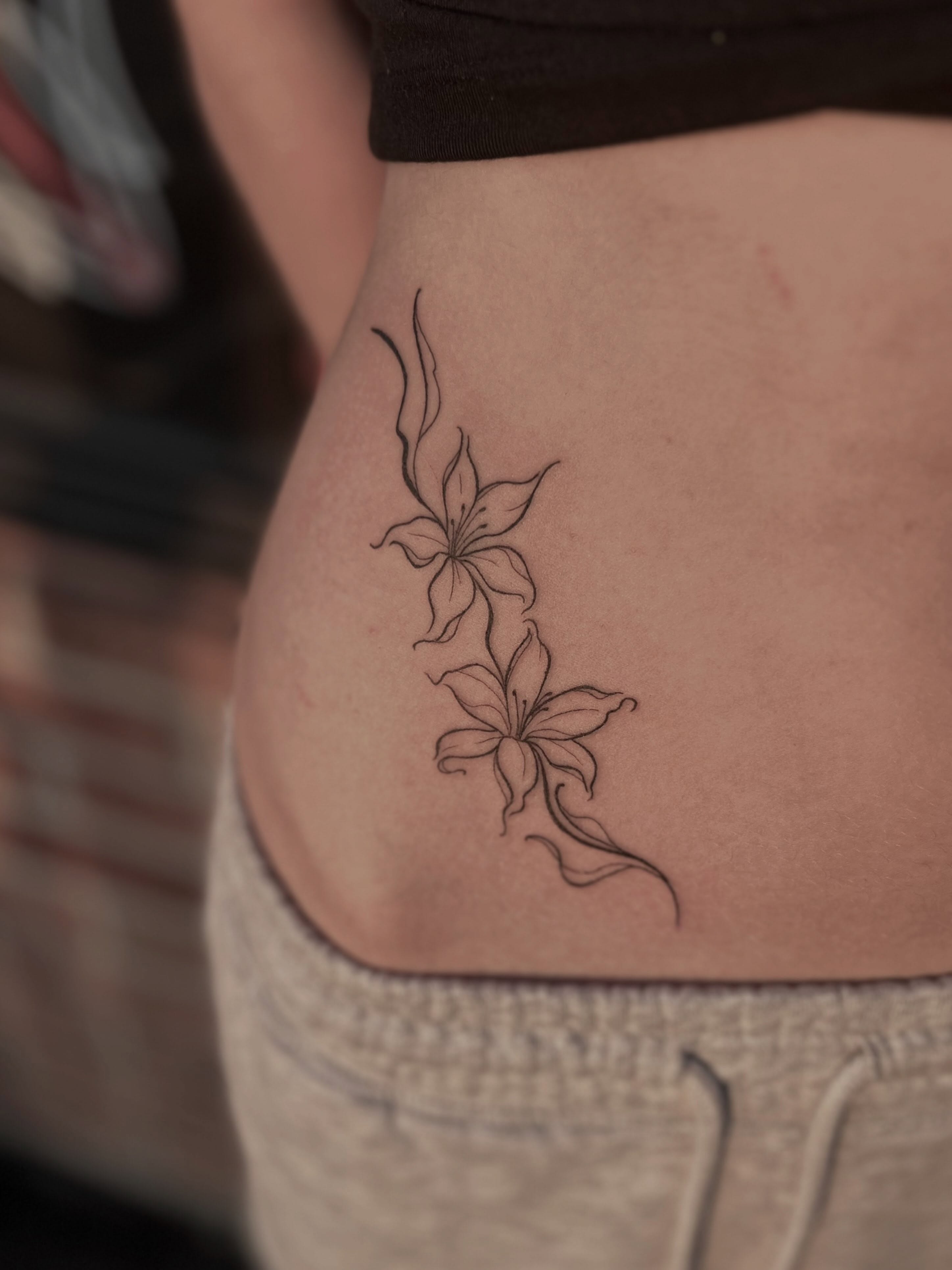 Lilies fine line tattoo on the thigh by Lexi Rose