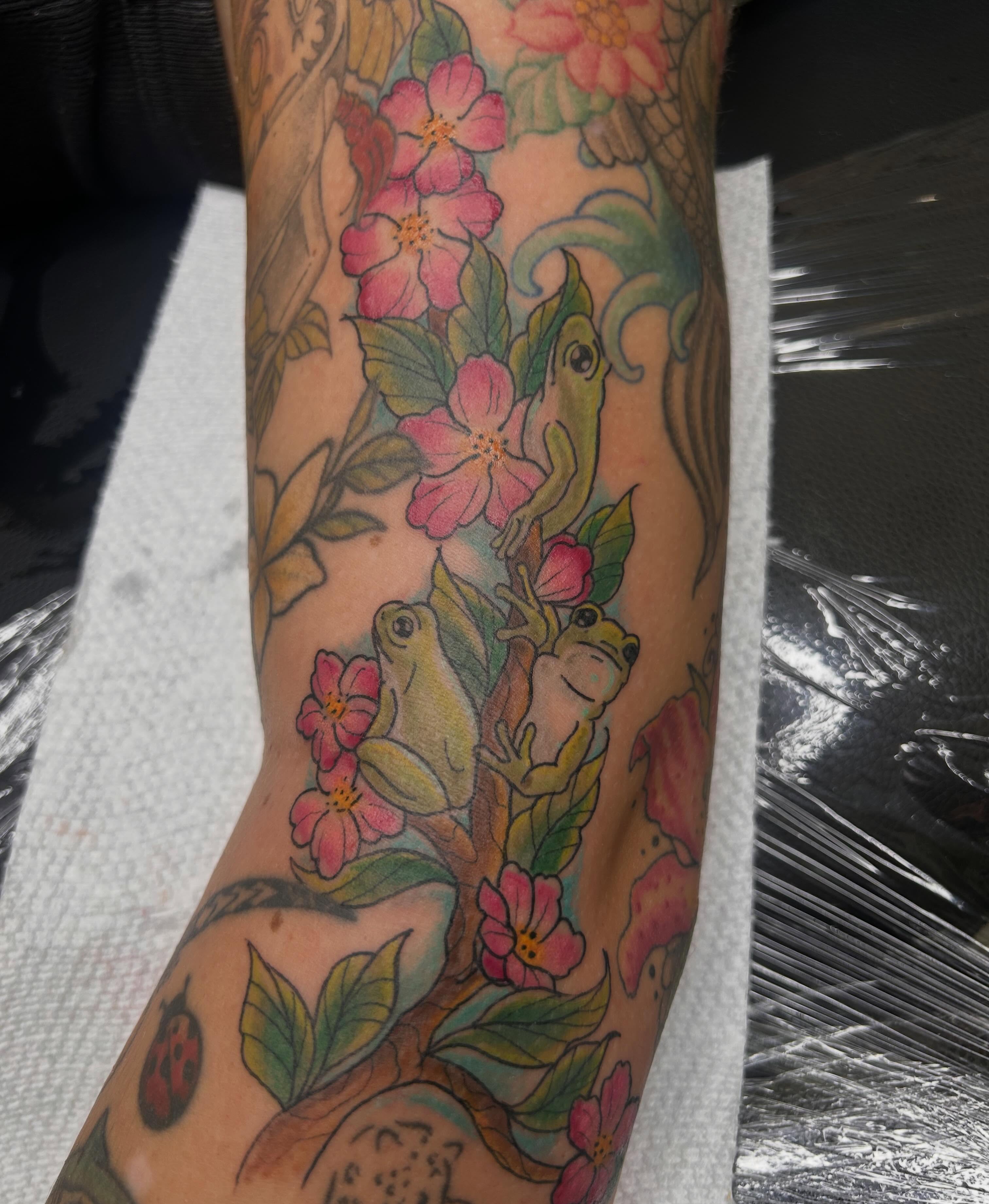 Frogs and flowers new school tattoo on the forearm by Reilley Earles