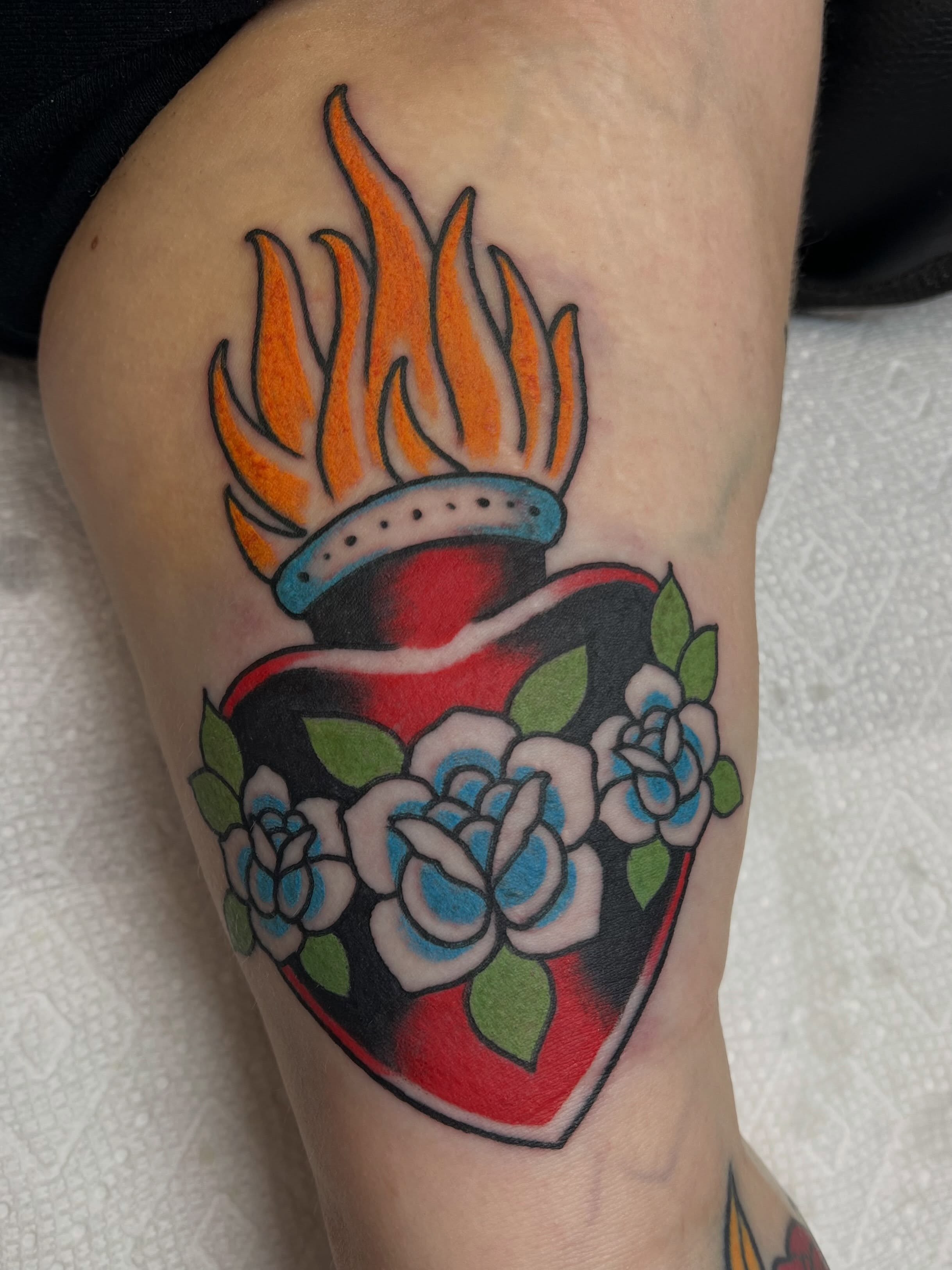 Flaming heart with roses American traditional tattoo on the thigh by Brandon McDaniel Iowa Tattoo Artist
