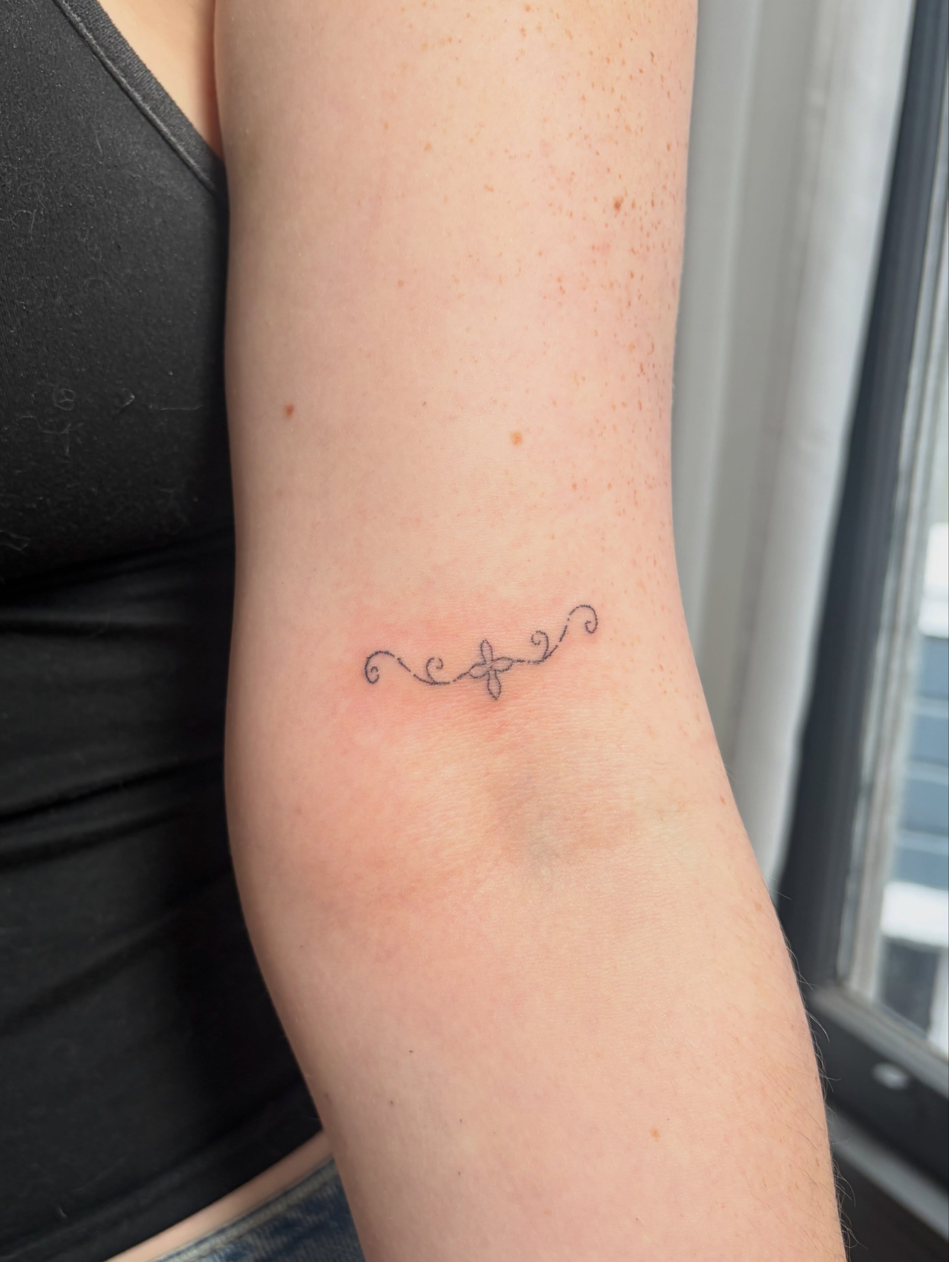 Cross with swirls fine line tattoo on the forearm by kari