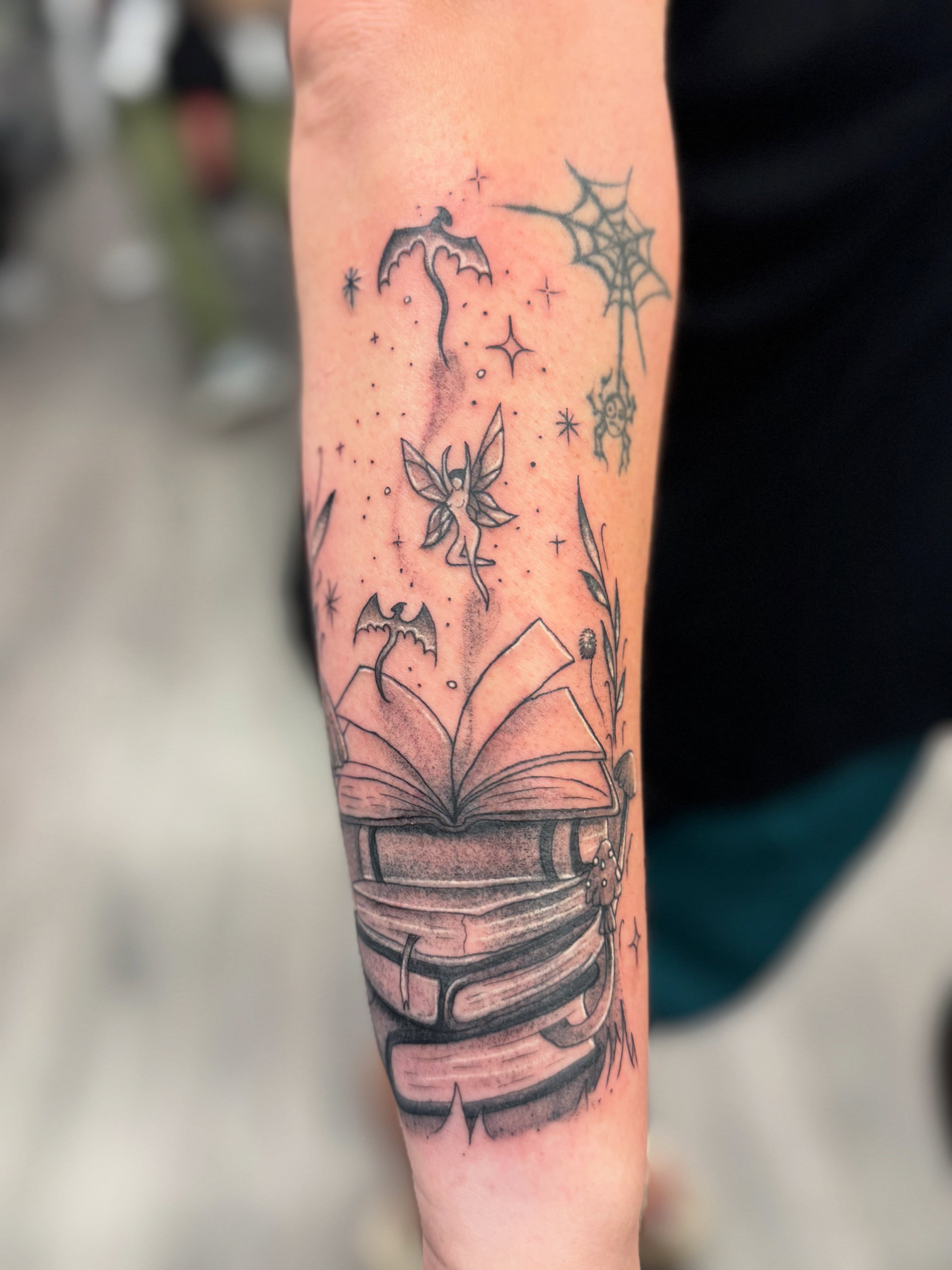 Open book with fairy dotwork tattoo on the forearm by Israel Jacob Woehler