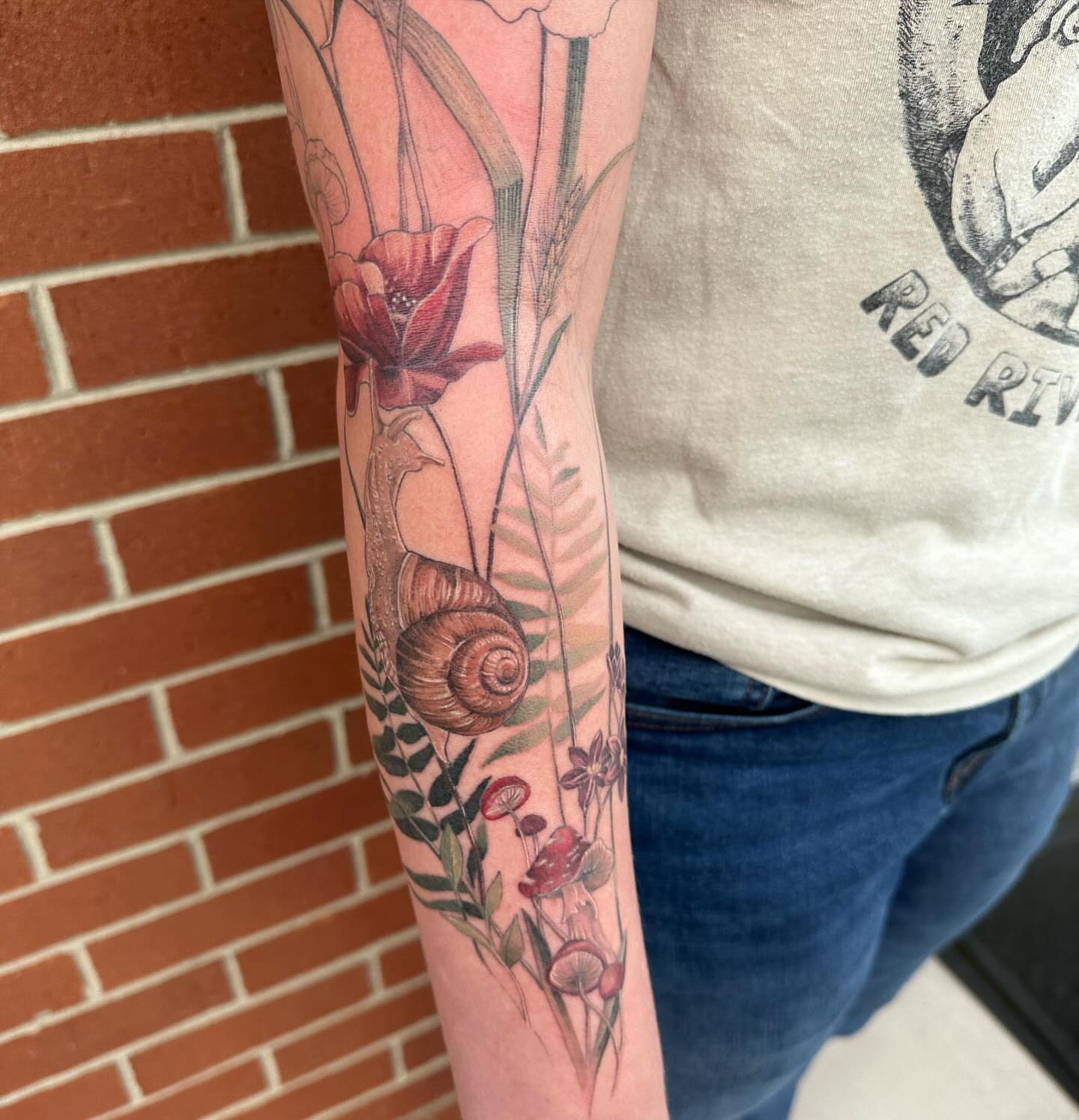 Snail and floral arrangement realism tattoo on the forearm by Cassandra Rasper-Beard