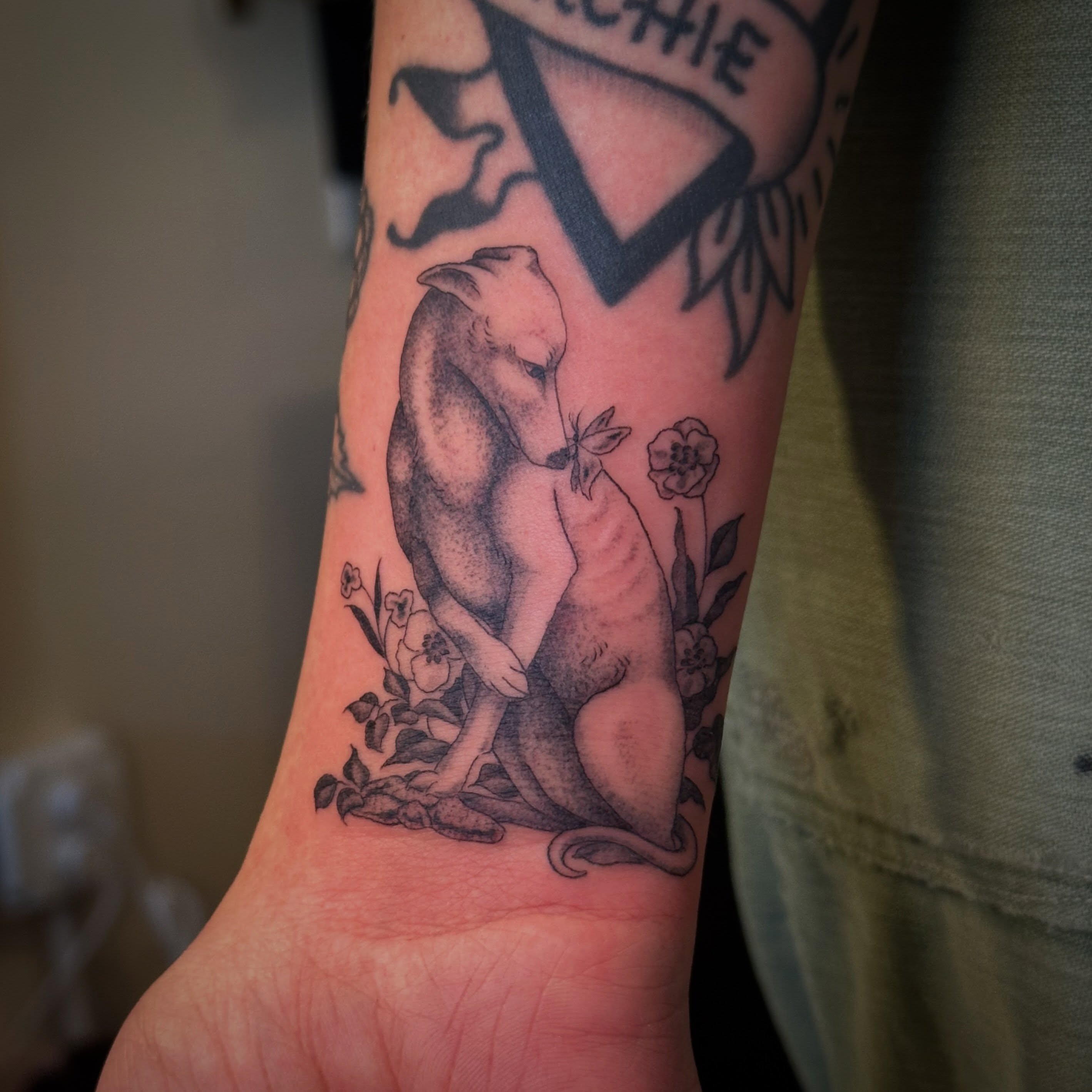Dog and flowers black and grey tattoo on the forearm by Bree Lin