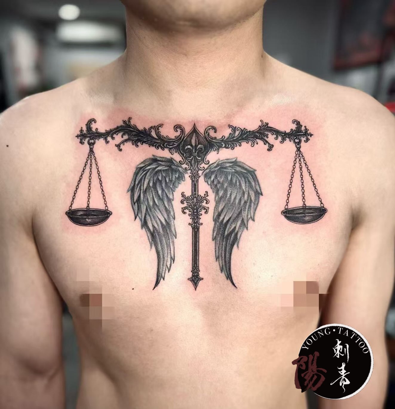 Balance scales and wings ornamental tattoo on the chest by Ying
