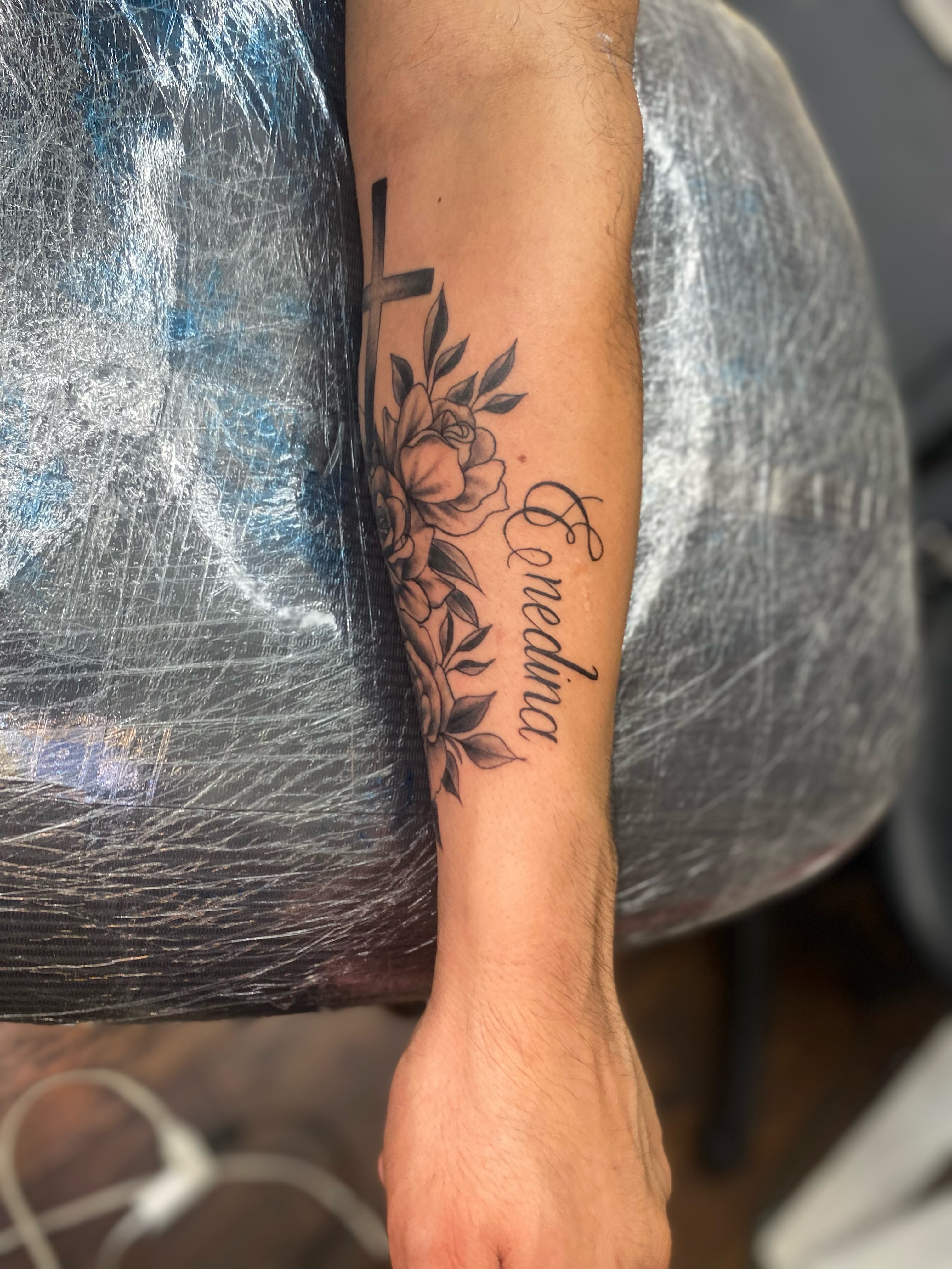 Cross and floral black and grey tattoo on the forearm by Irving Guzman