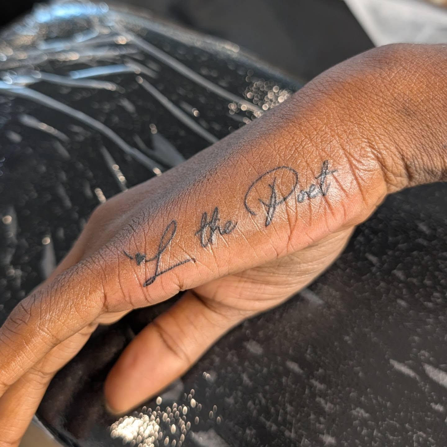 L the Poet lettering script tattoo on the hand by Nenookaasi Martin