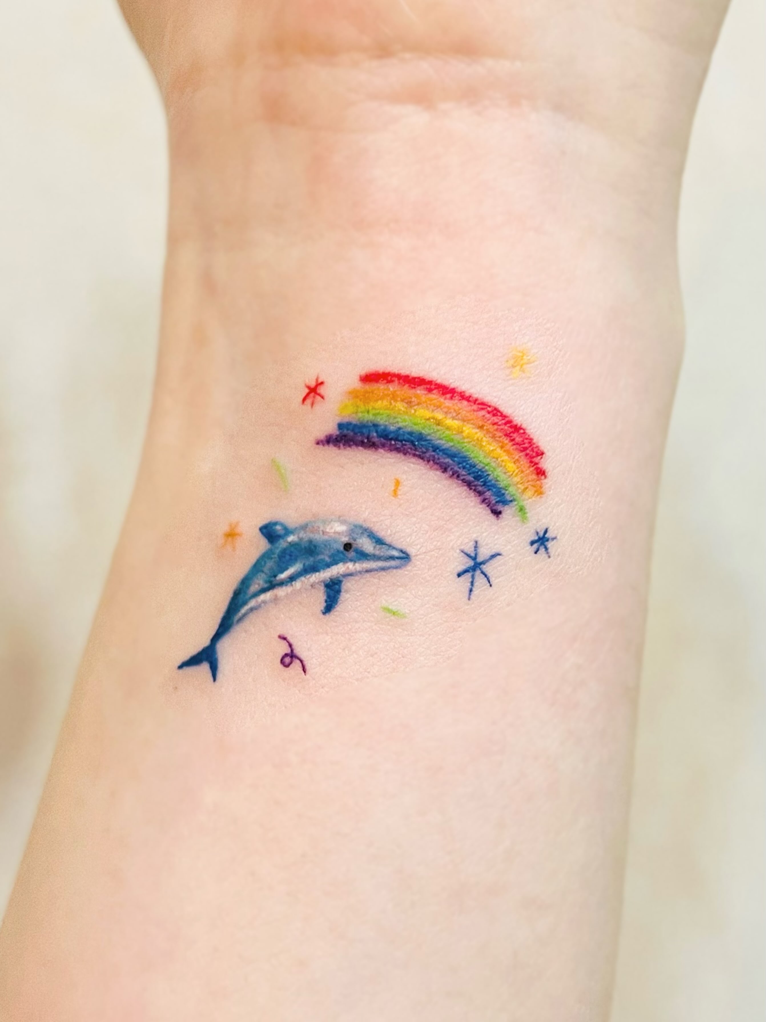 Dolphin and rainbow watercolor tattoo on the forearm by Purinn