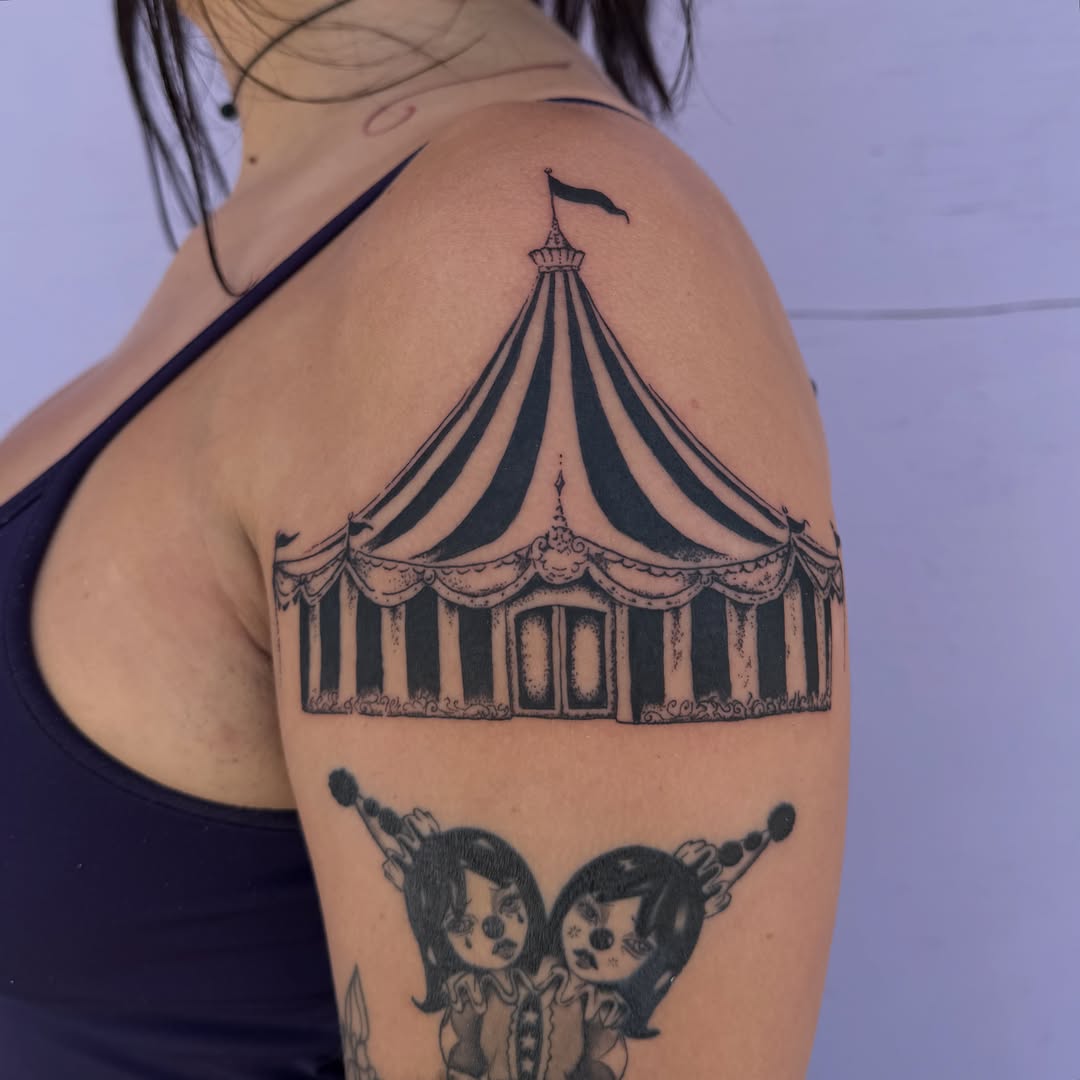 Circus tent and clowns black and grey tattoo on the shoulder by Sophia Tattoo