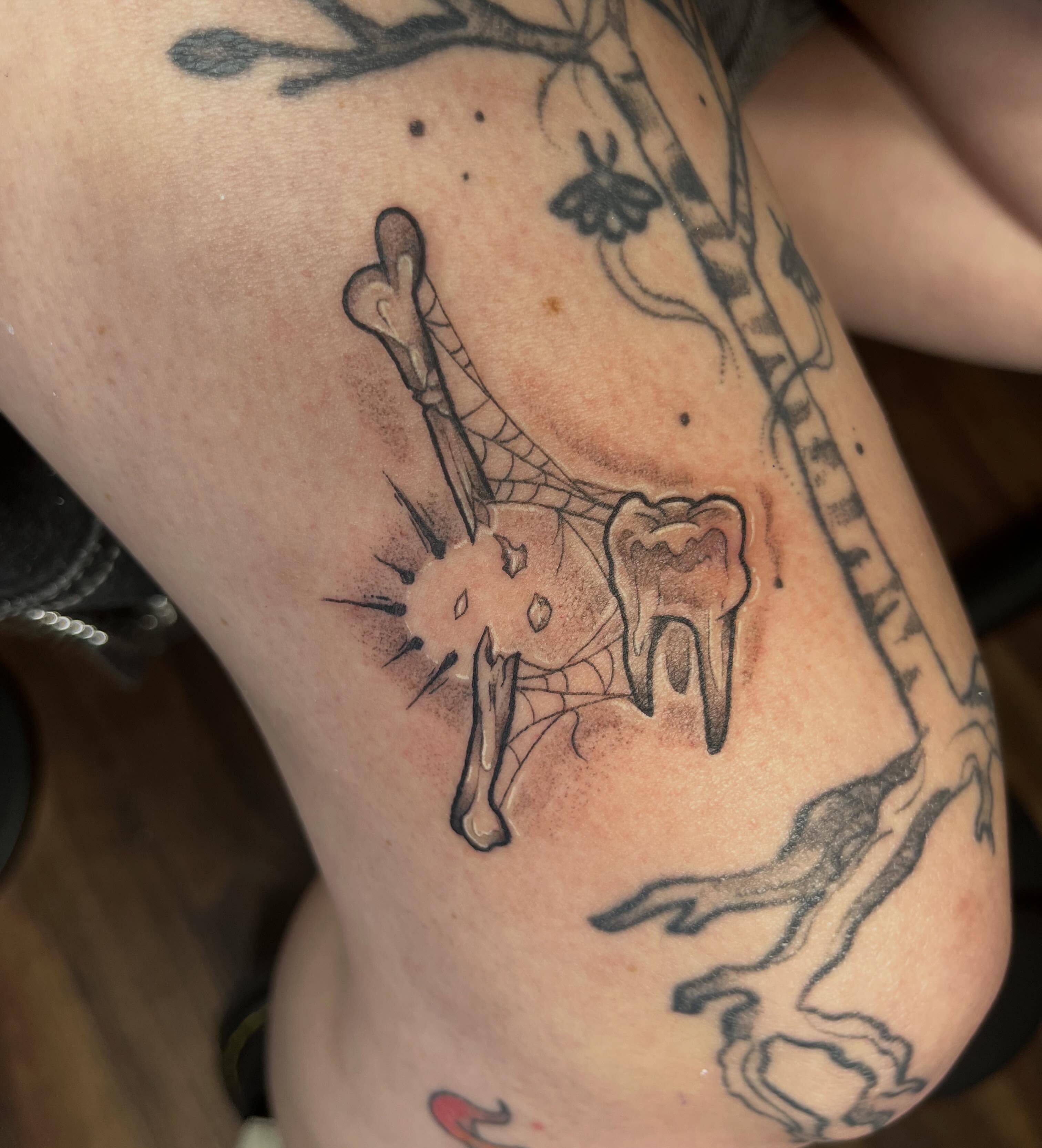 Tooth and bone black and grey tattoo on the thigh by Jazzy