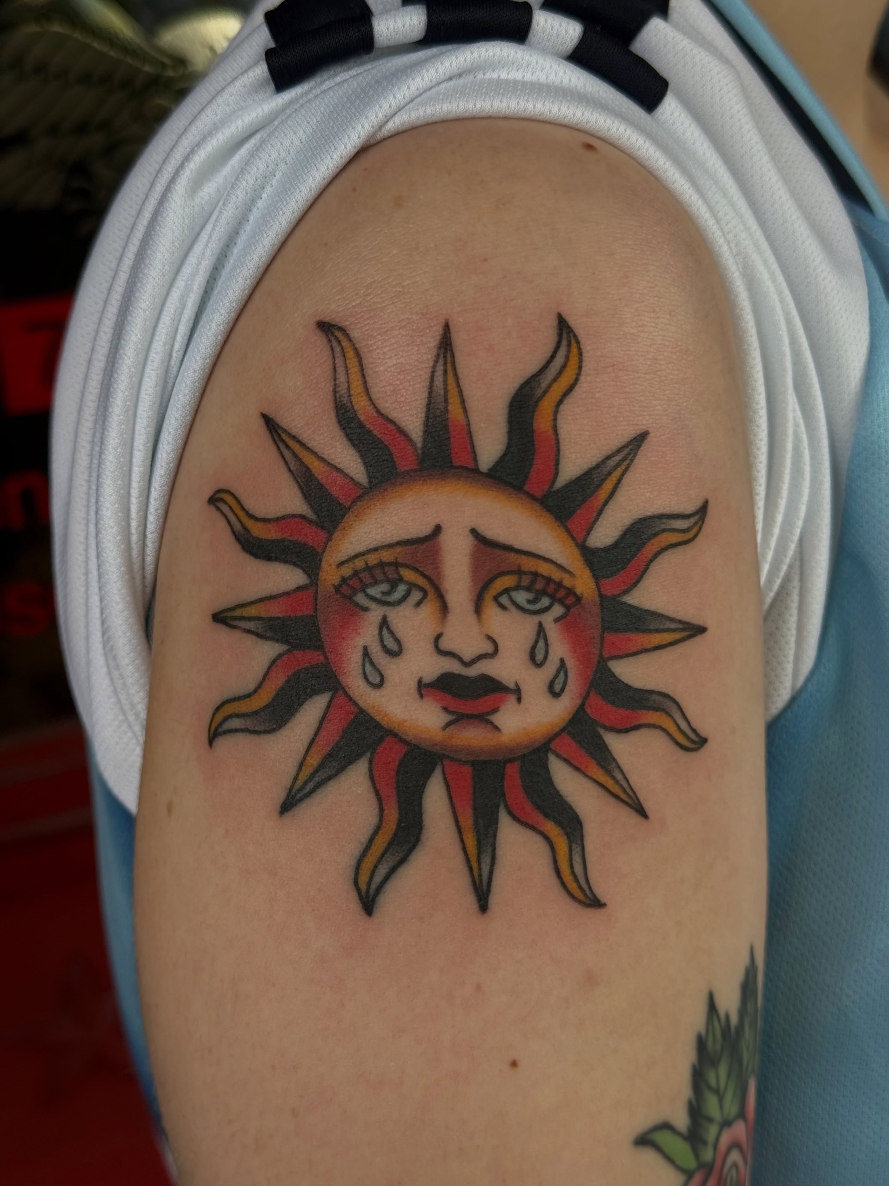 Sad sun American traditional tattoo on the shoulder by Kaysen