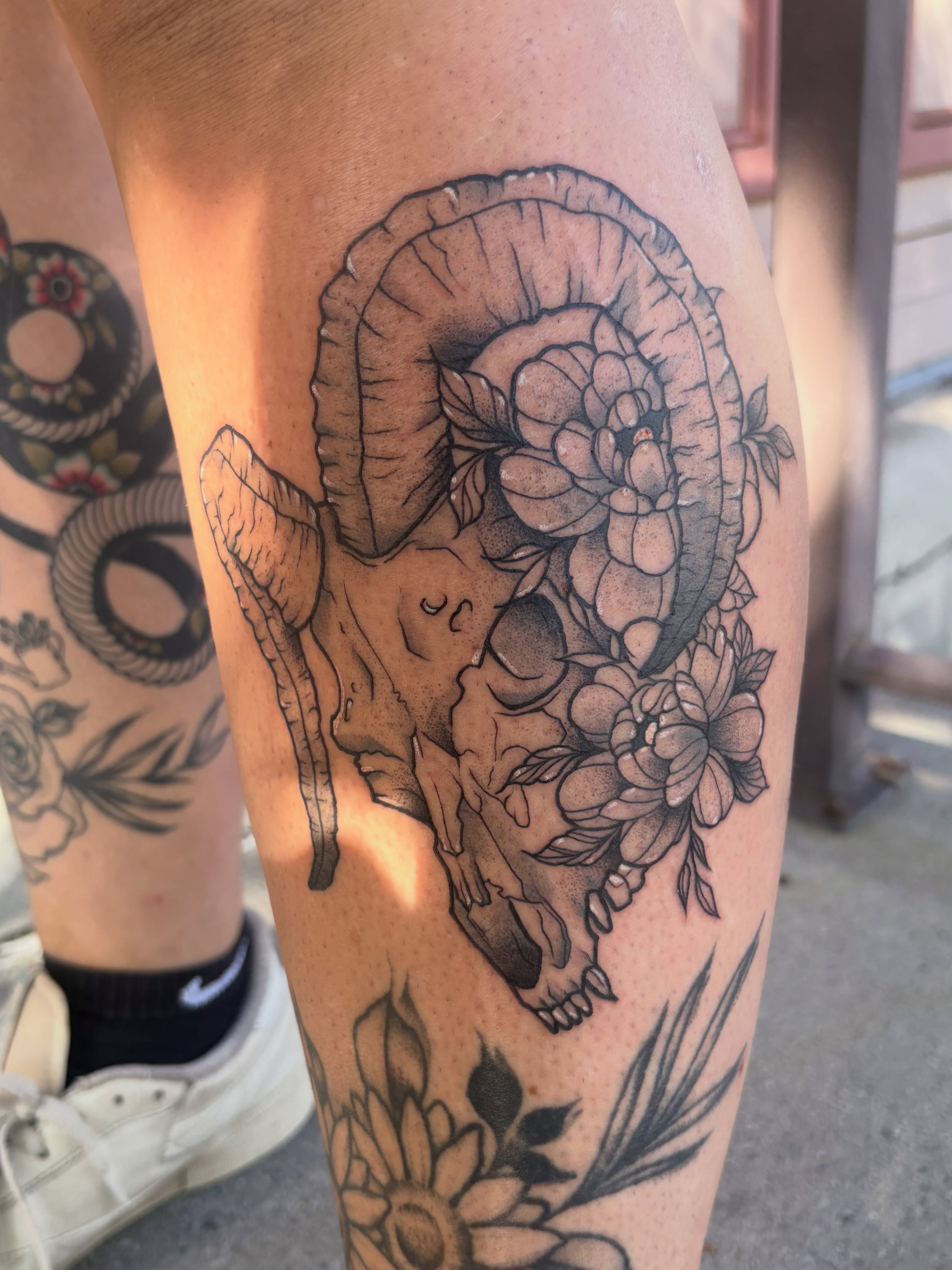 Ram skull with flowers black and grey tattoo on the thigh by Liz Cook