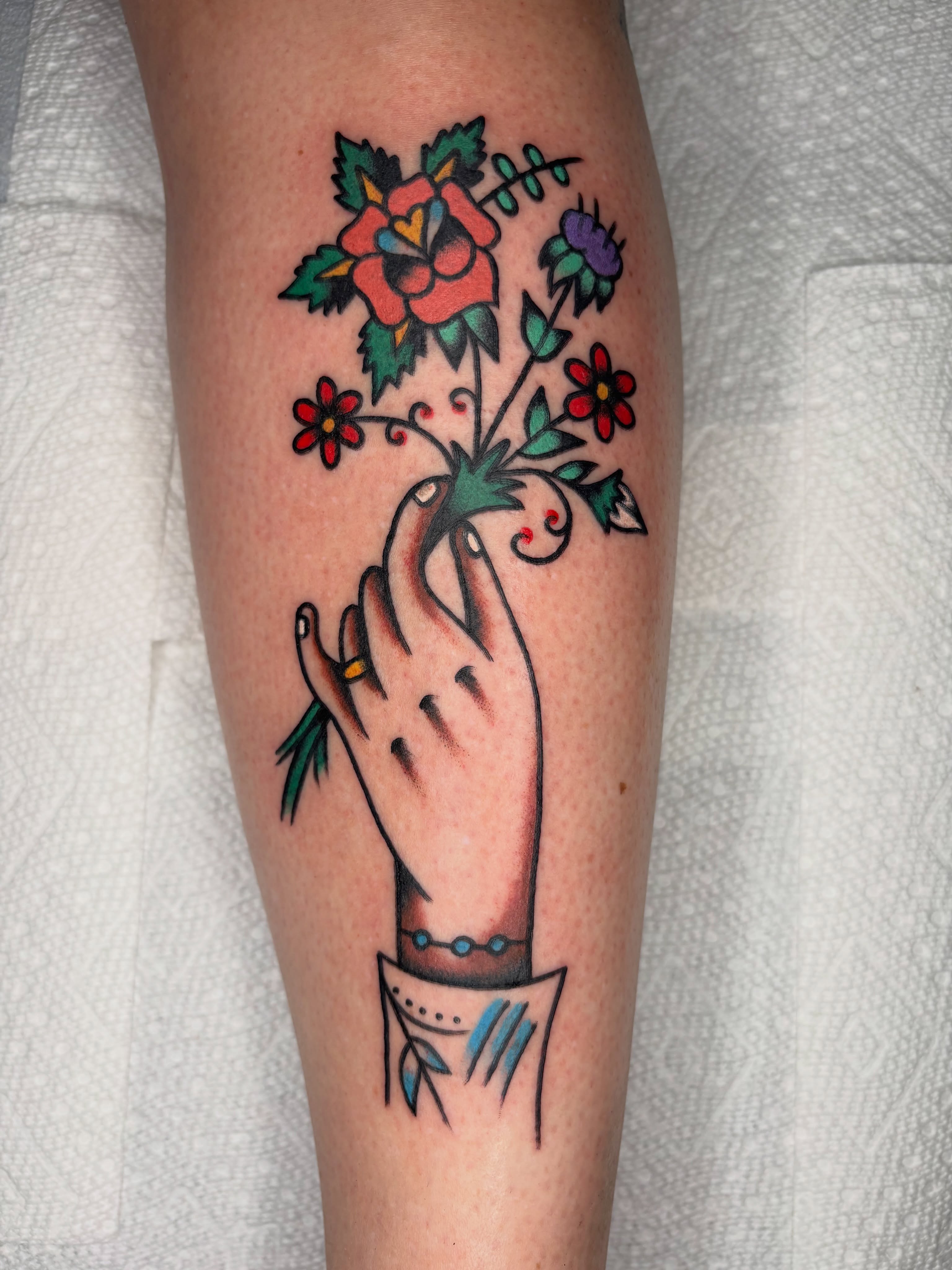 Hand holding flowers American traditional tattoo on the forearm by Cooper Reichwein