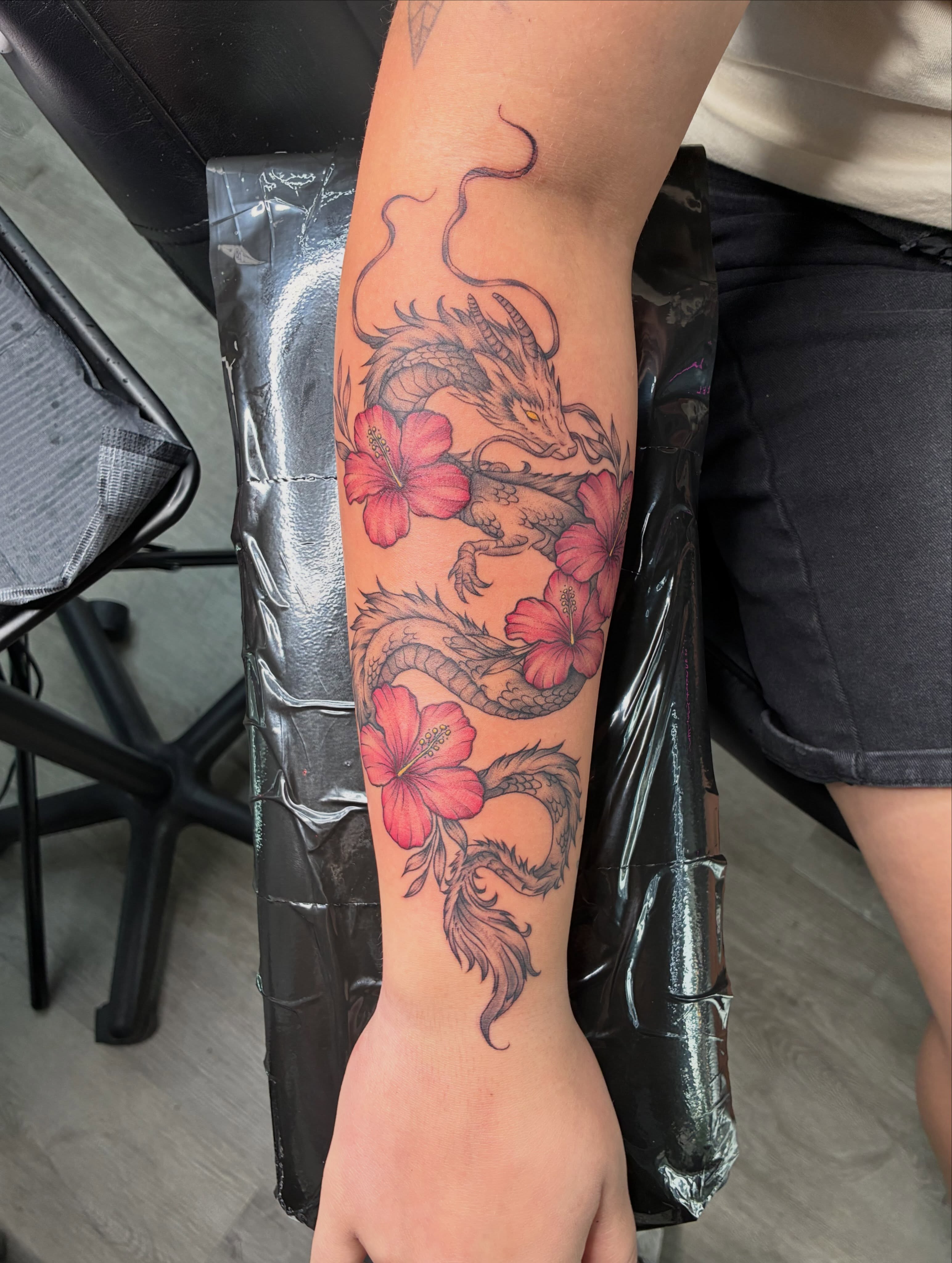 Dragon and hibiscus black and grey tattoo on the forearm by Tattoos by Hailey