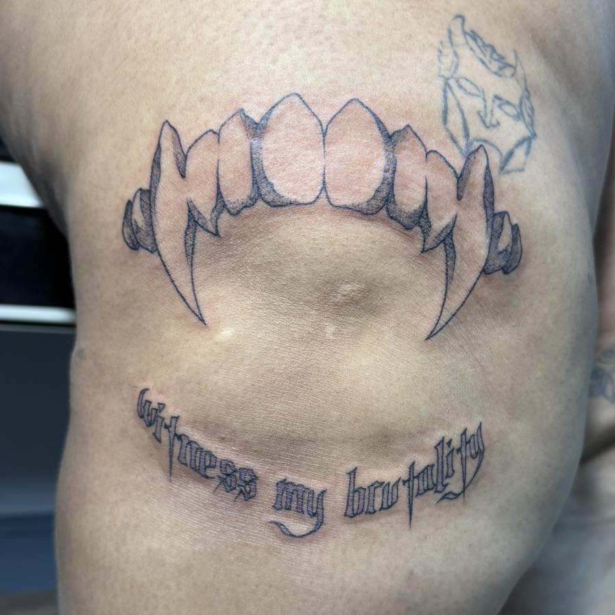 Fangs and text black and grey tattoo on the chest by Destiny A