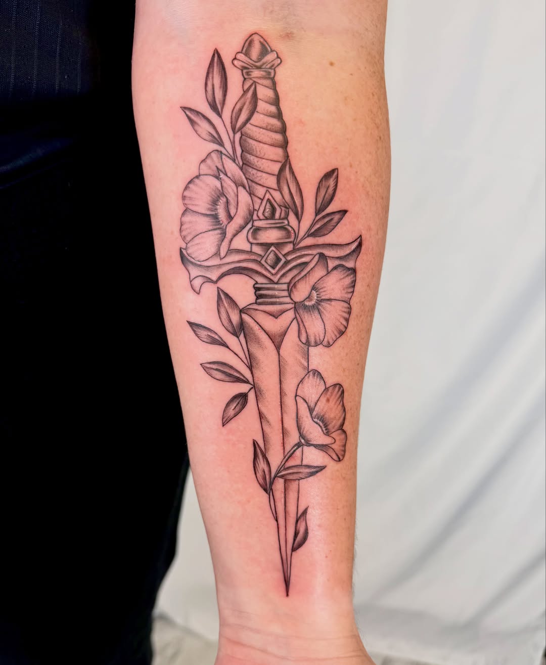 Sword and flowers black and grey tattoo on the forearm by Jerry Thomas