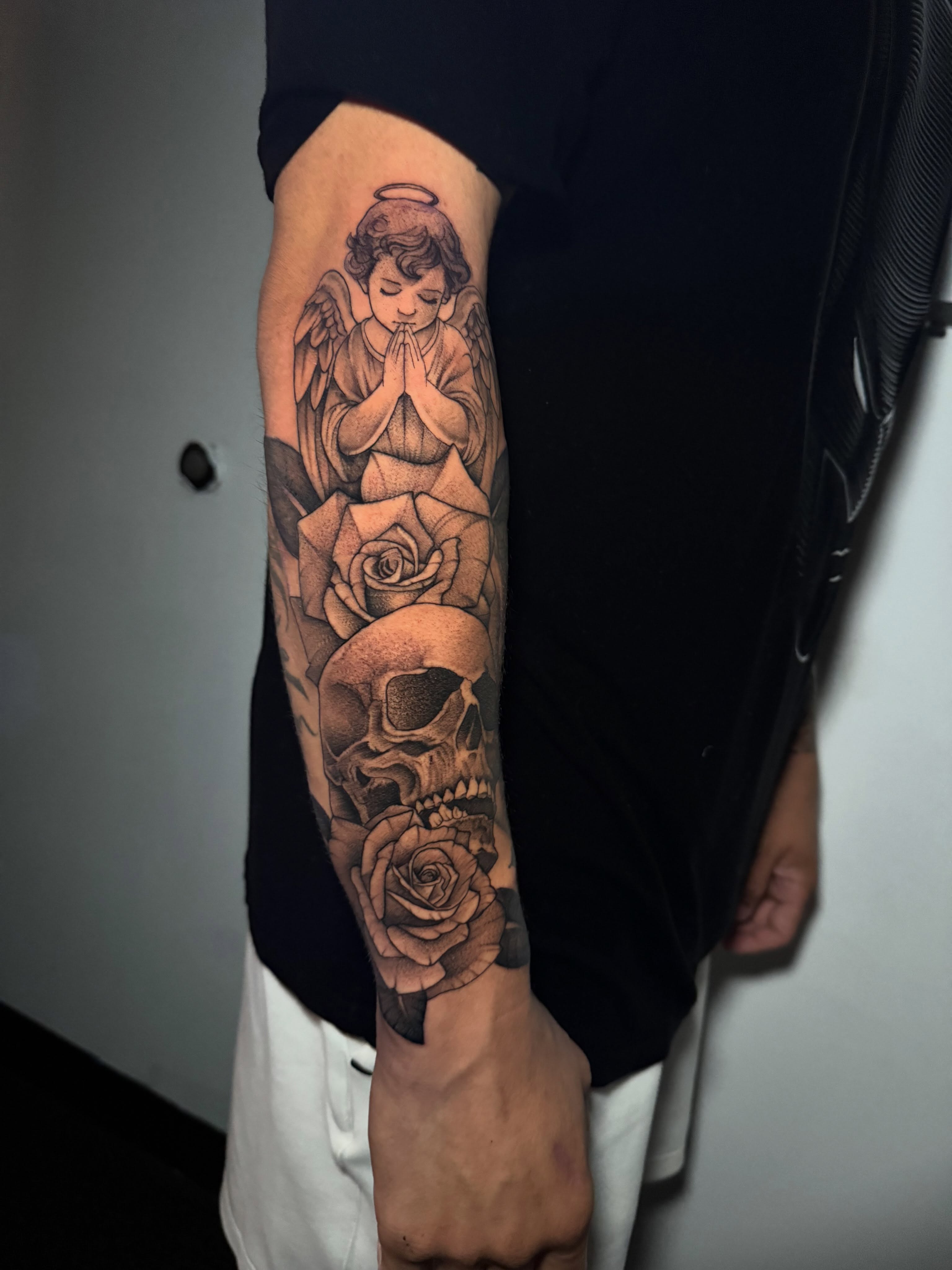 Angel praying with roses and skull realism tattoo on the forearm by Lindsay