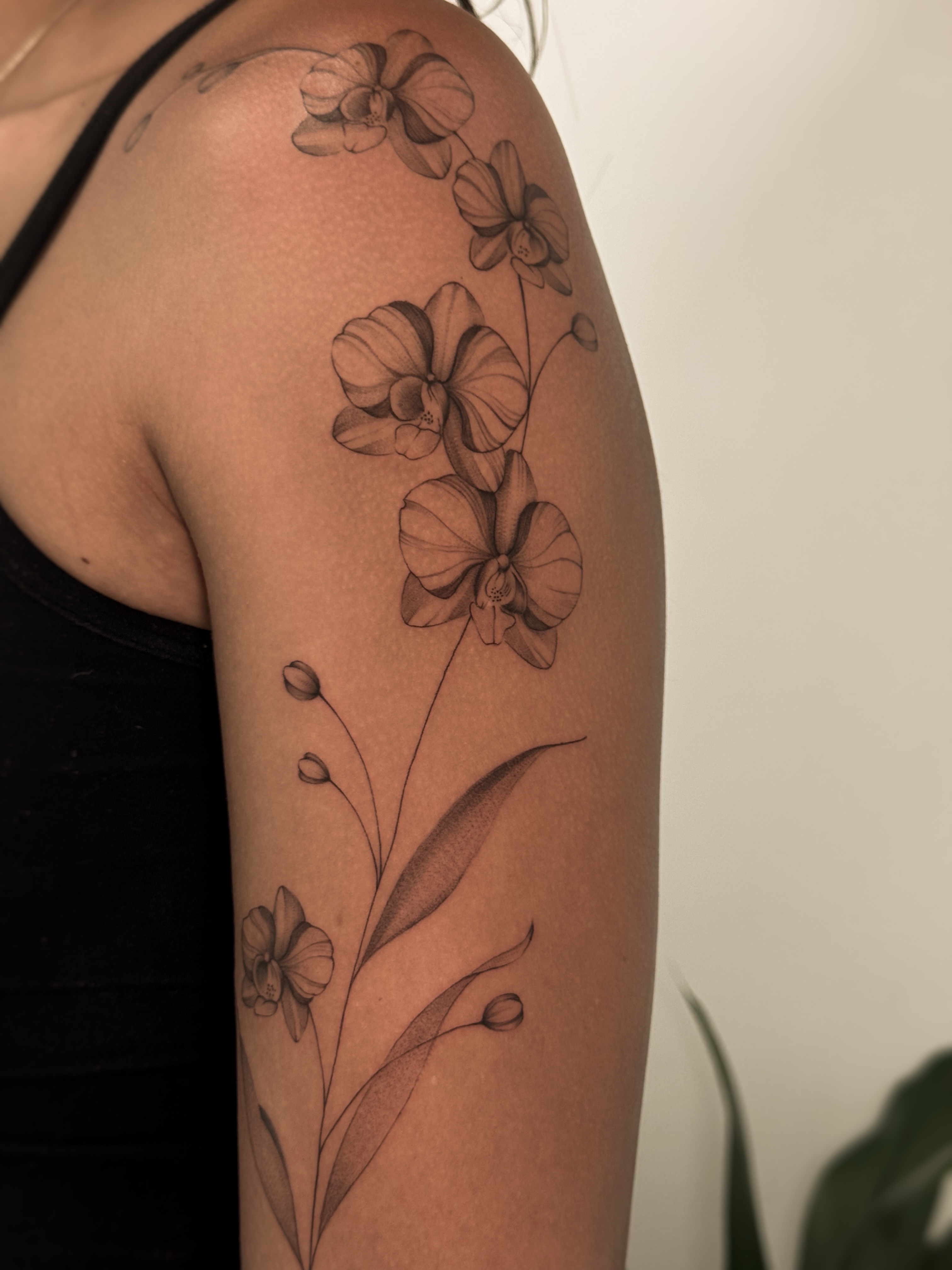 Orchids black and grey tattoo on the upper arm by Gianna Rodriguez