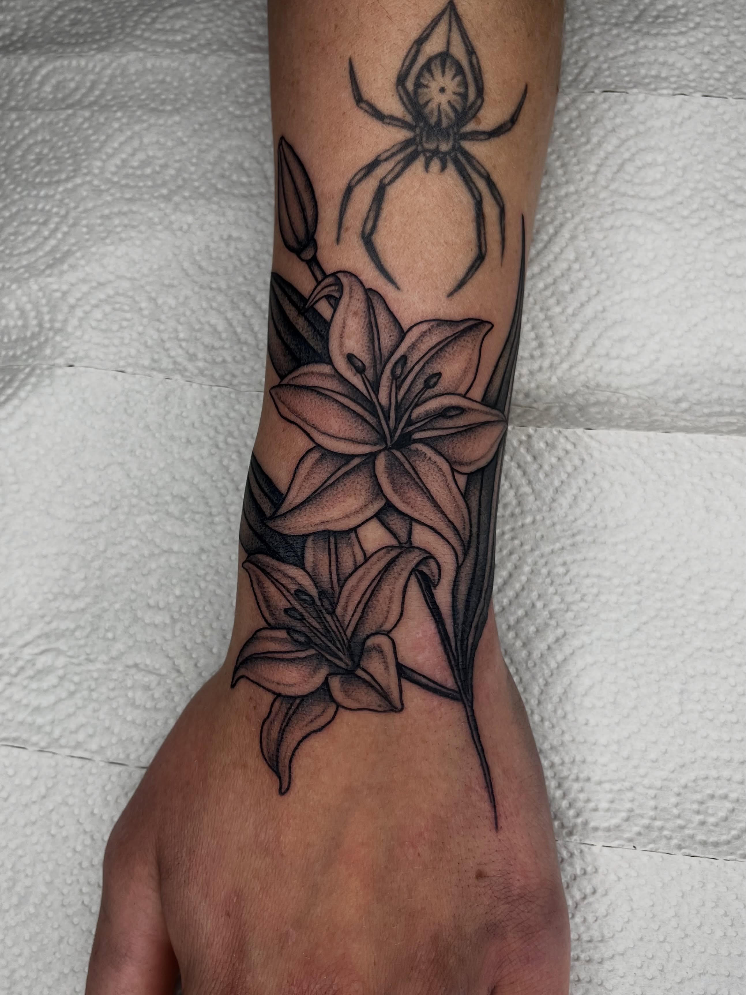 Lilies and spider black and grey tattoo on the forearm by Patrick Elijah