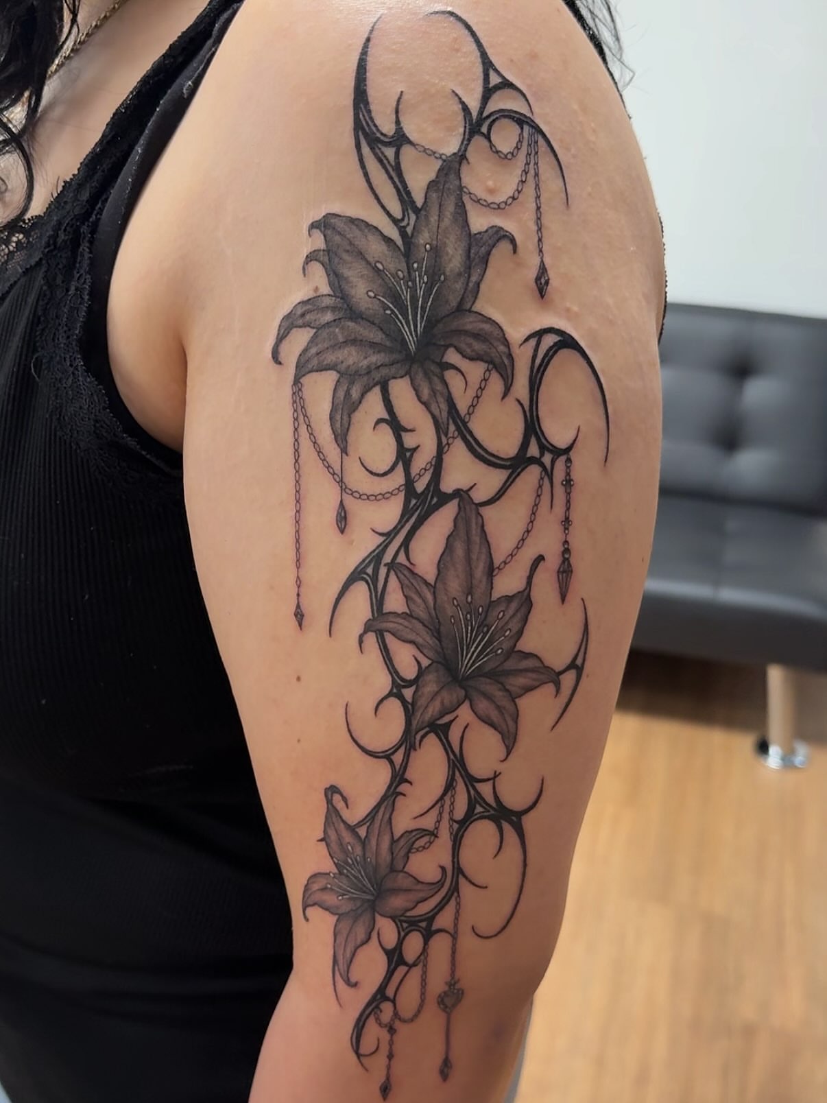 Lily black and grey tattoo on the upper arm by Royal Martinez