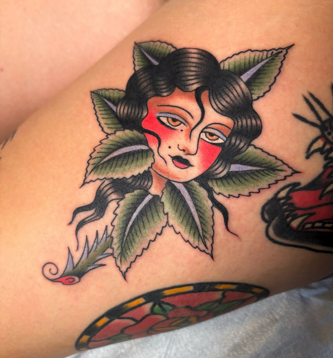 Woman with leaves American traditional tattoo on the thigh by Caeli Martin