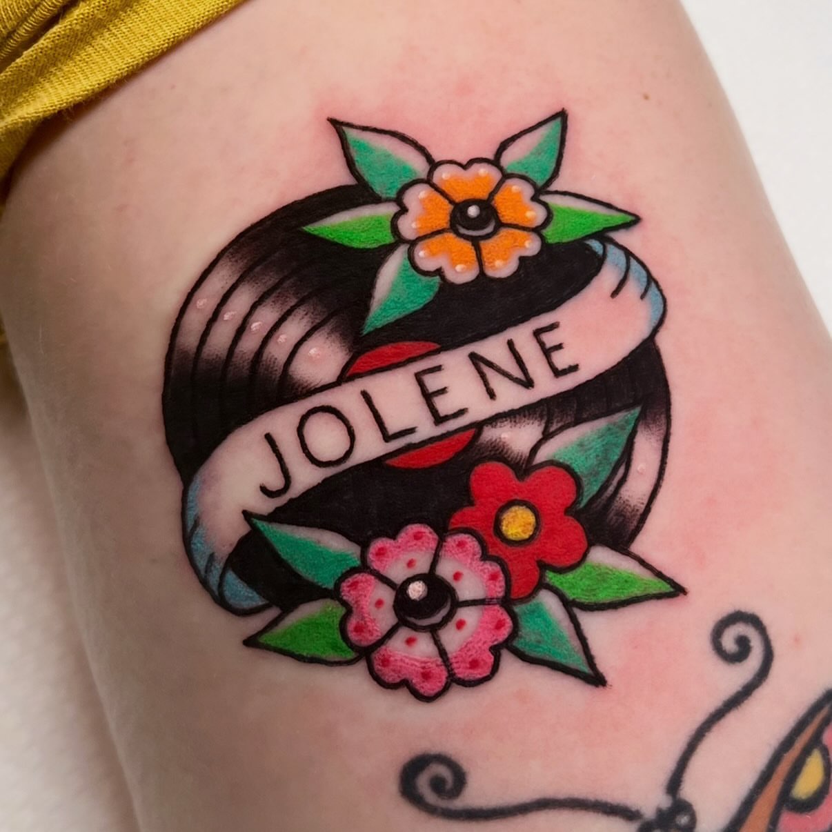 Flower and ribbon American traditional tattoo on the upper arm by Alena McDonald