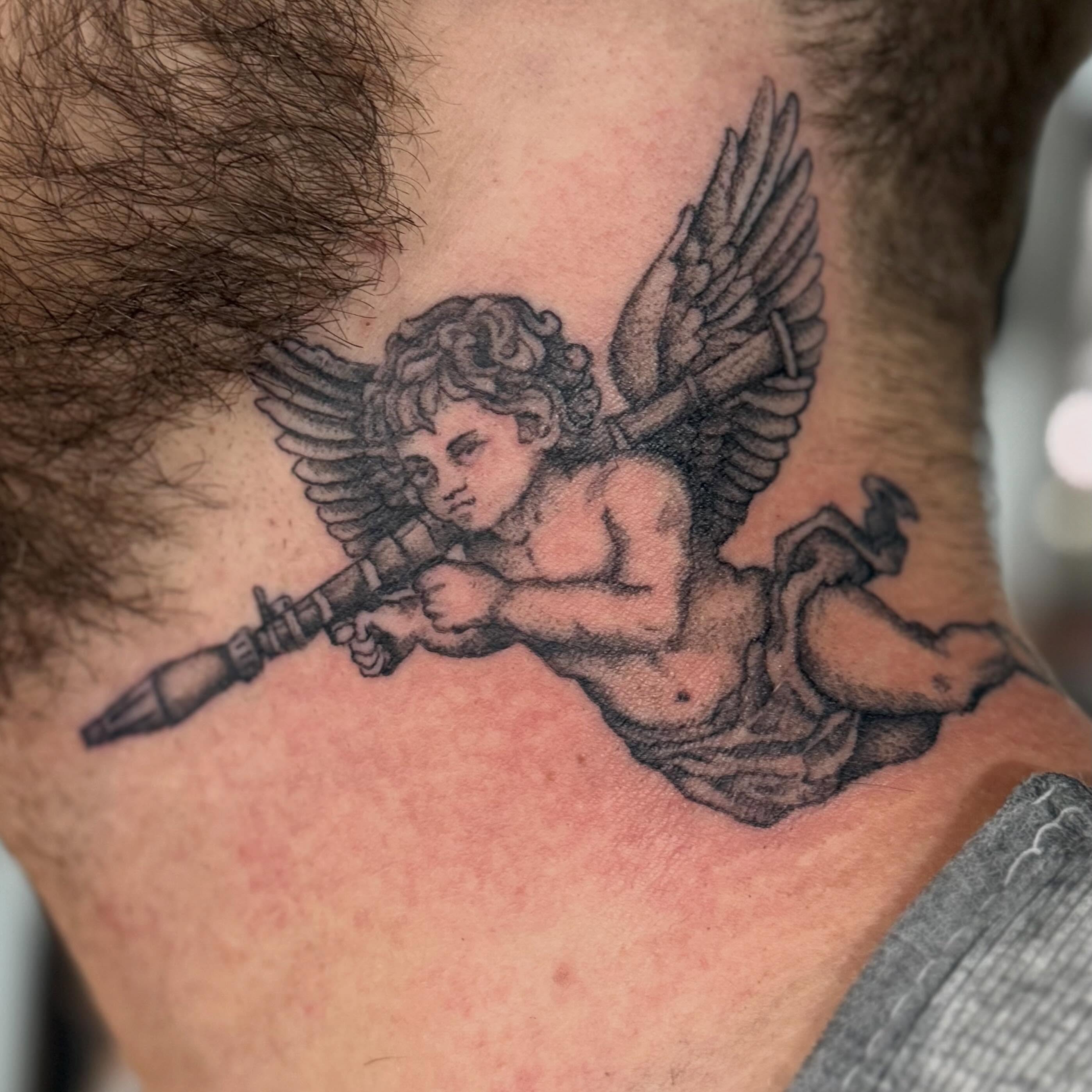 Cherub with gun black and grey tattoo on the neck by Tony Beuke