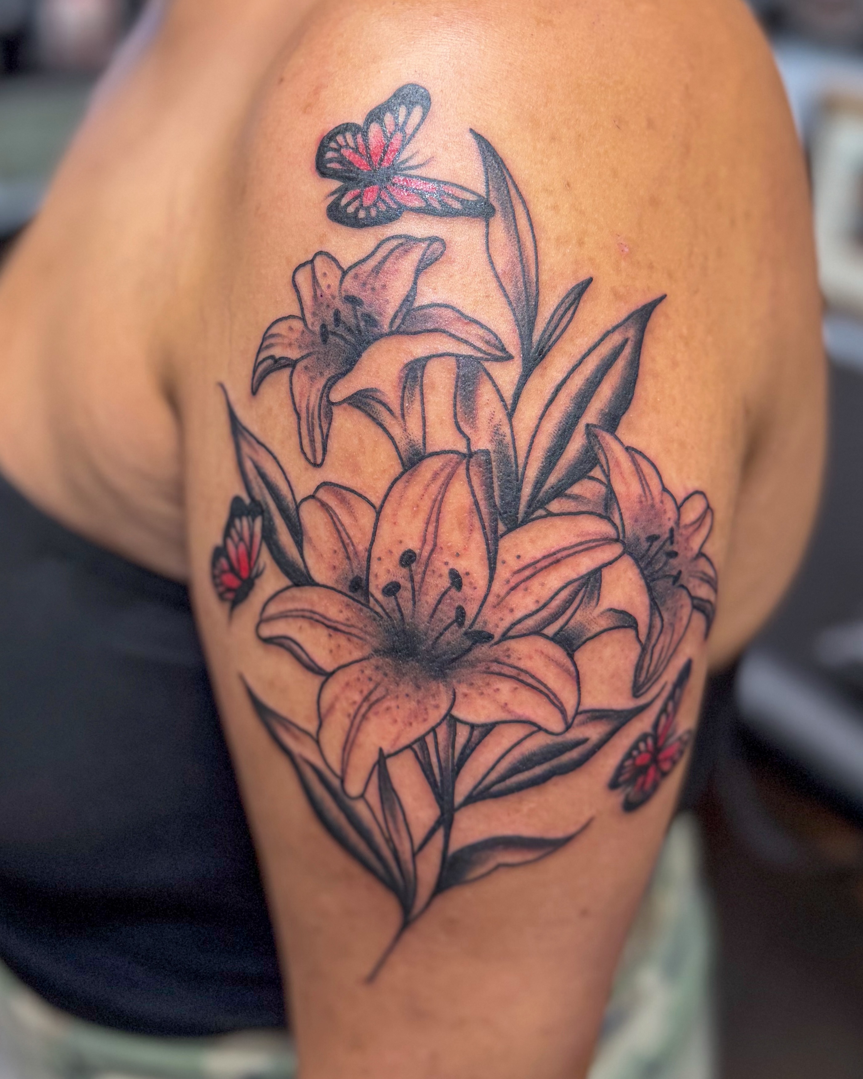 Lilies and butterfly black and grey tattoo on the shoulder by Zac Tattooer