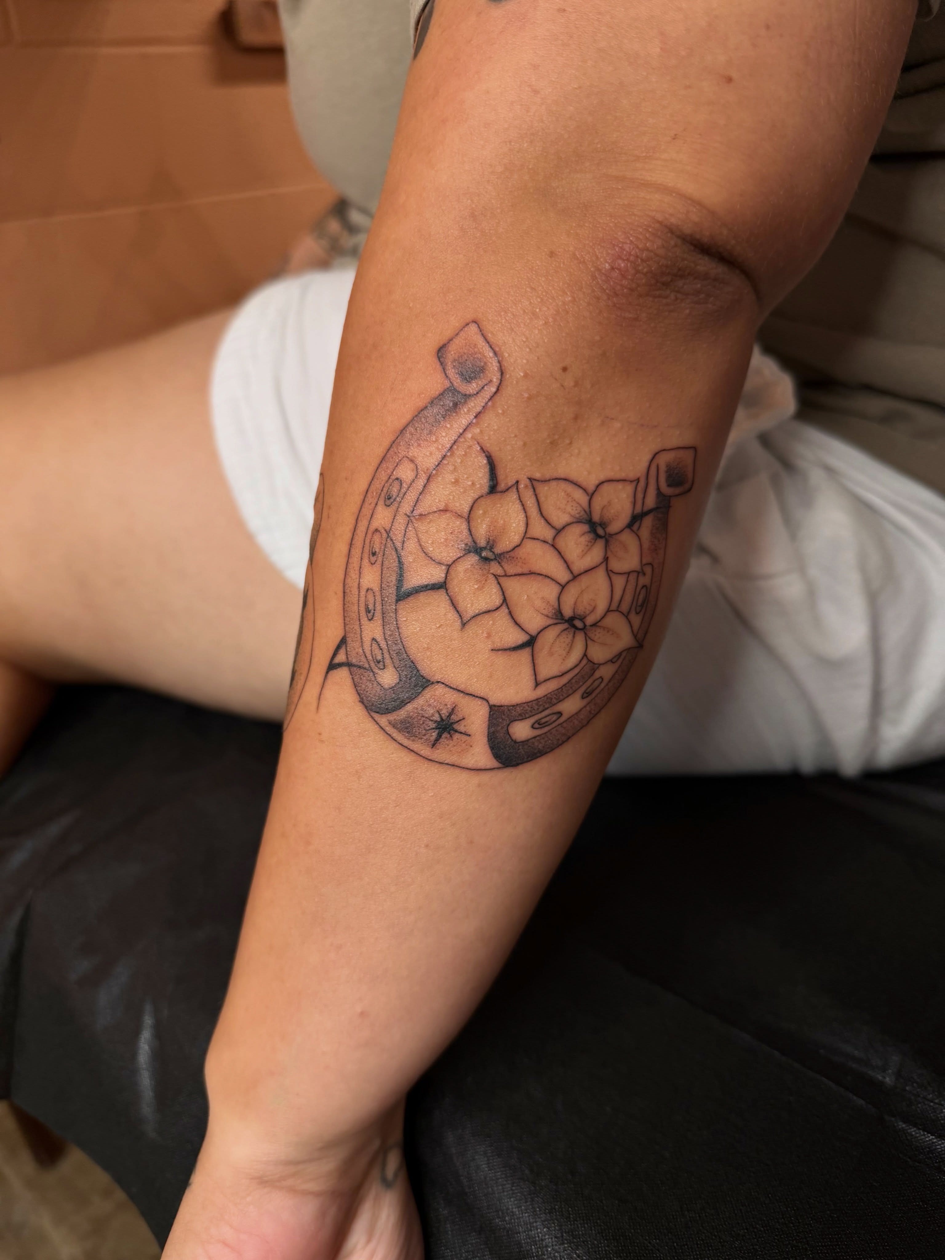 Horseshoe with flowers black and grey tattoo on the forearm by christian martinez