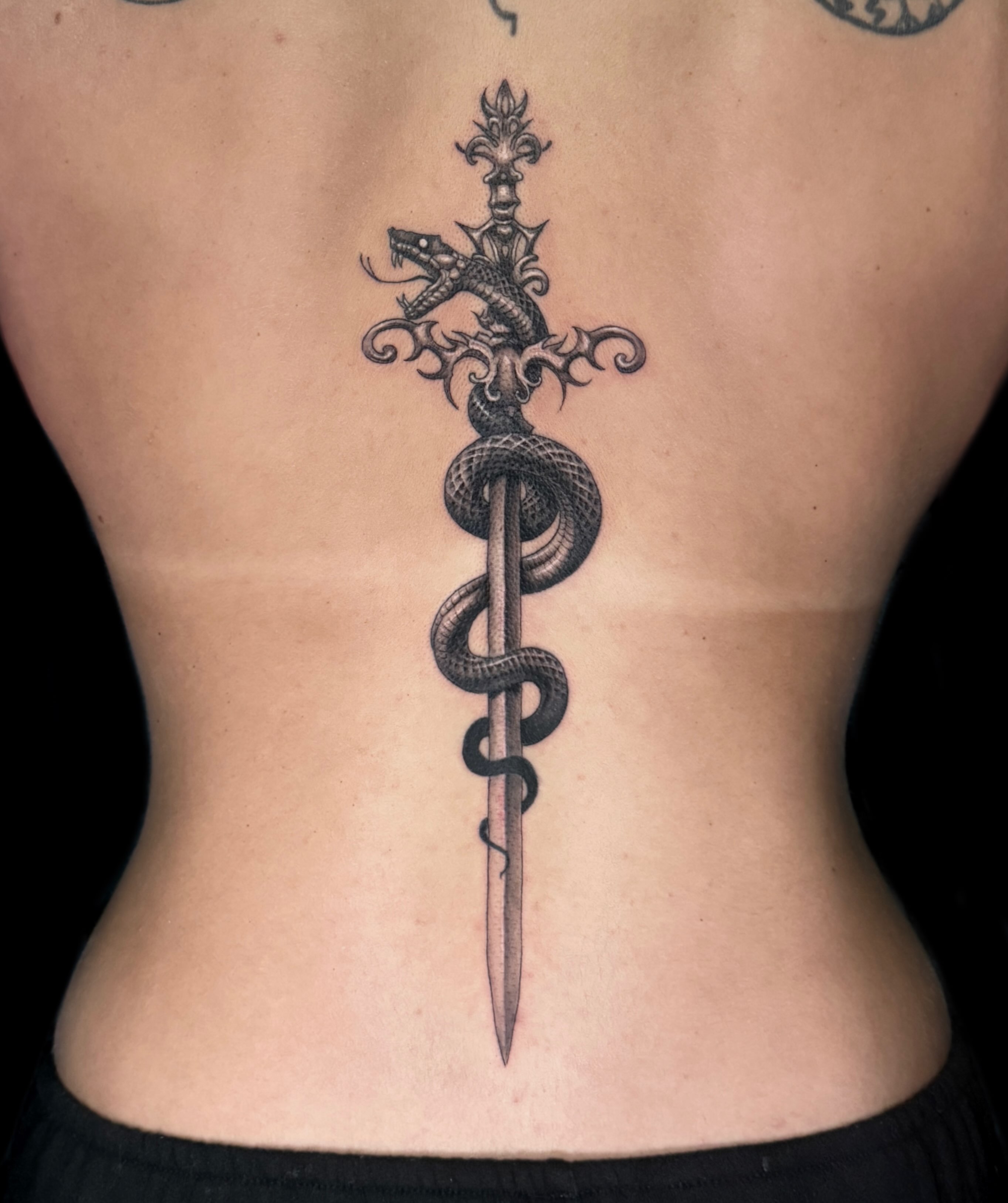 Snake and dagger geometric tattoo on the back by Madeleine Fleming