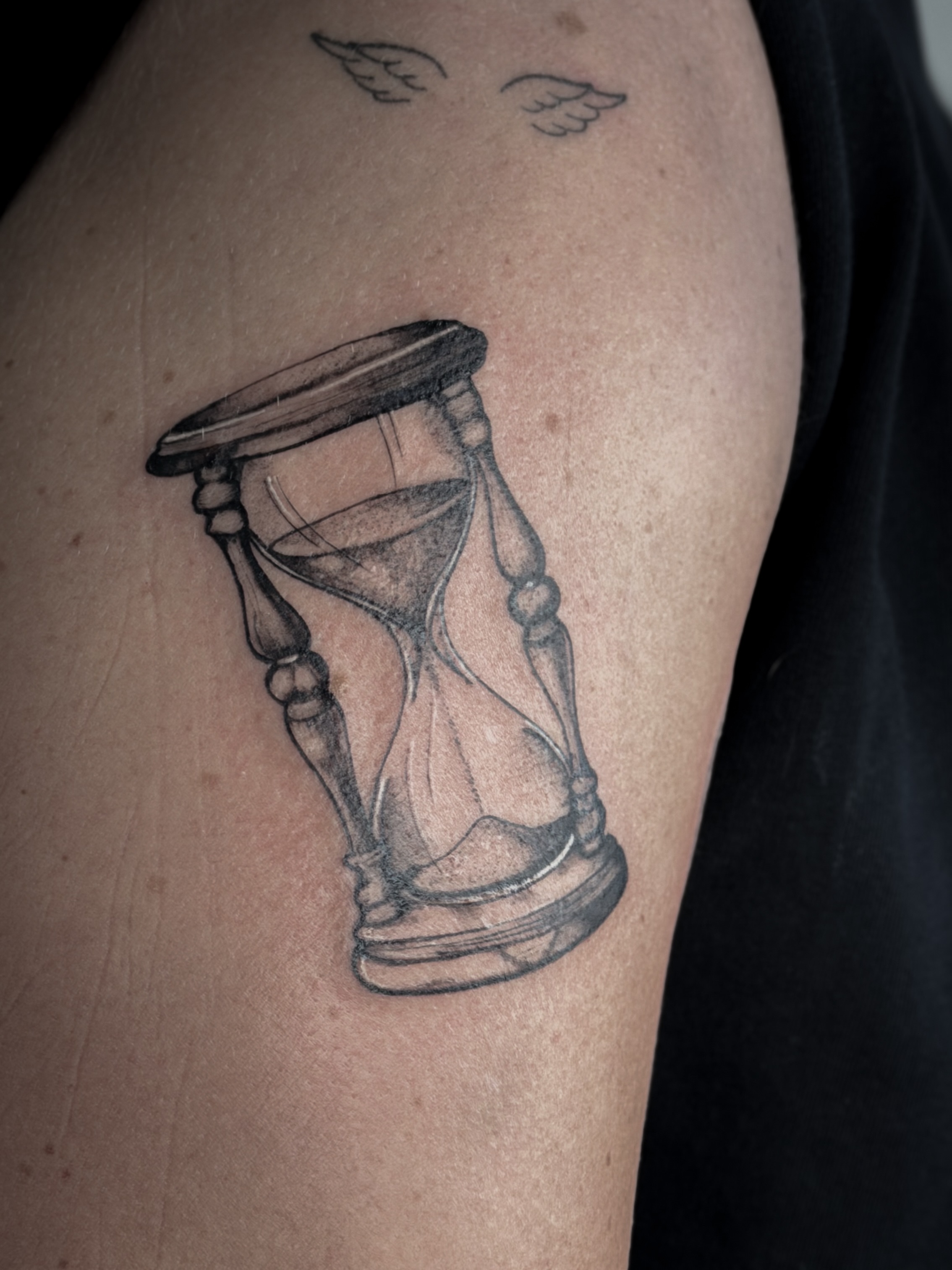 Hourglass black and grey tattoo on the upper arm by Tatuajes Denver