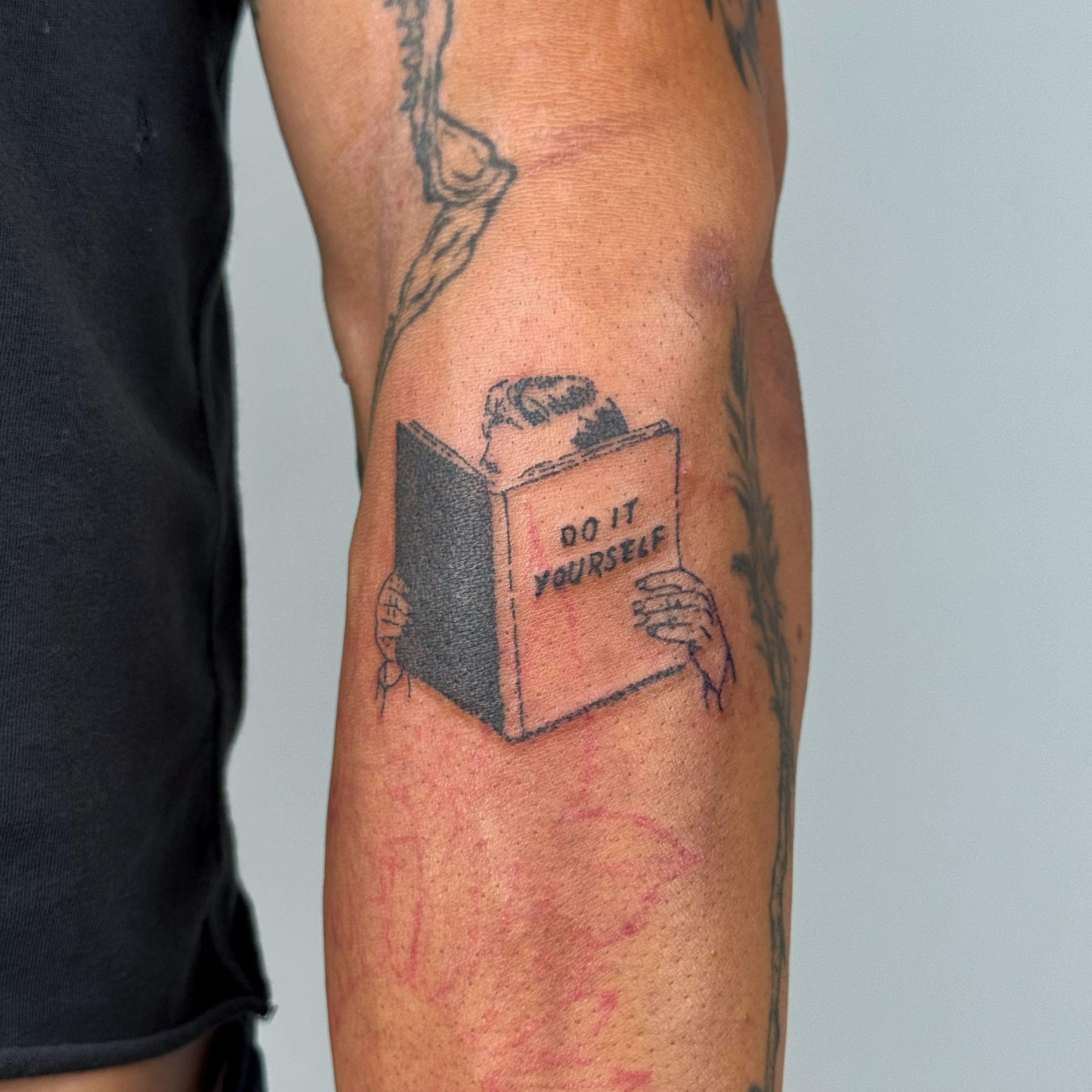 Book with text black and grey tattoo on the forearm by Joint Killer