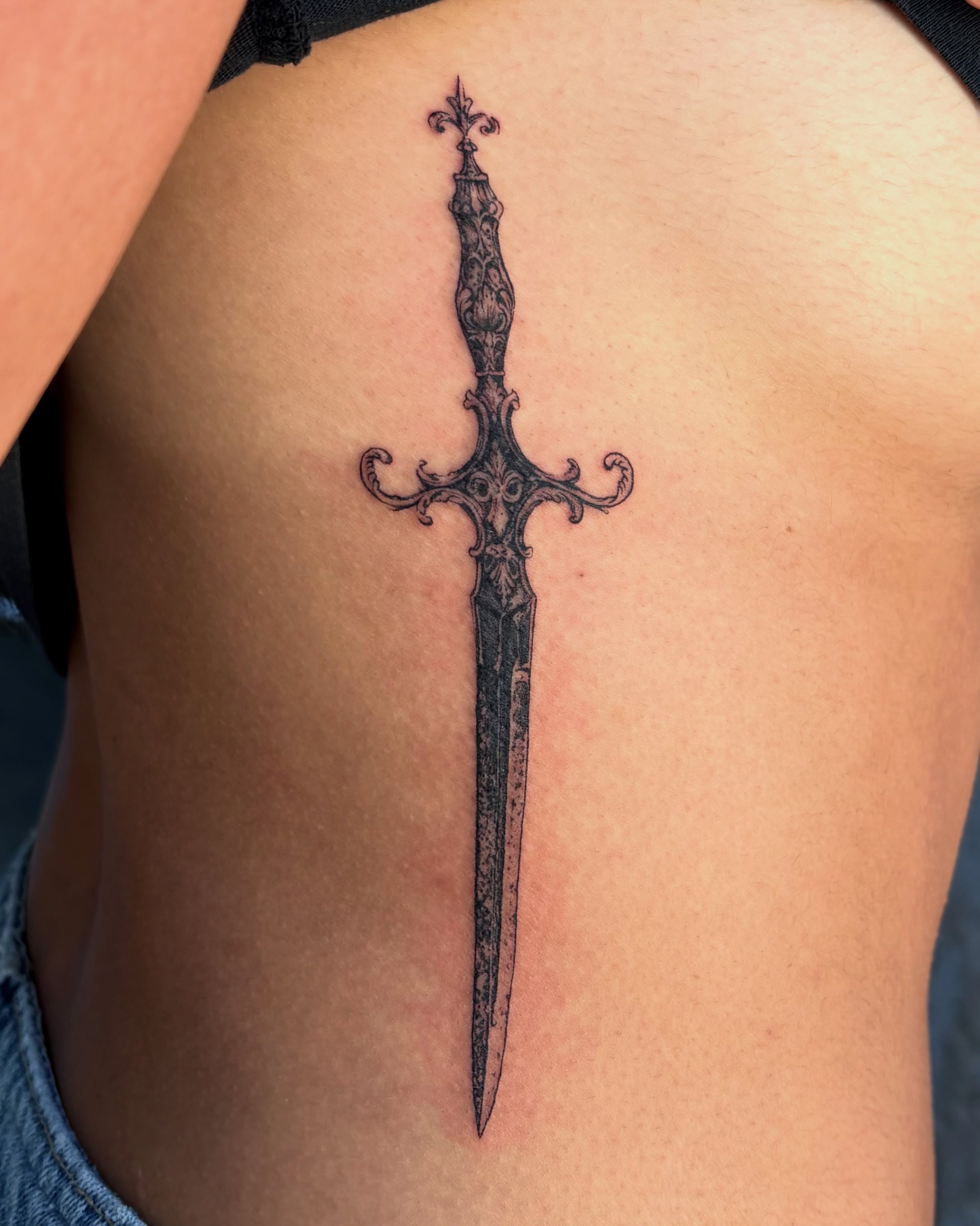 Sword black and grey tattoo on the ribs by Kylah Amin Tattoo