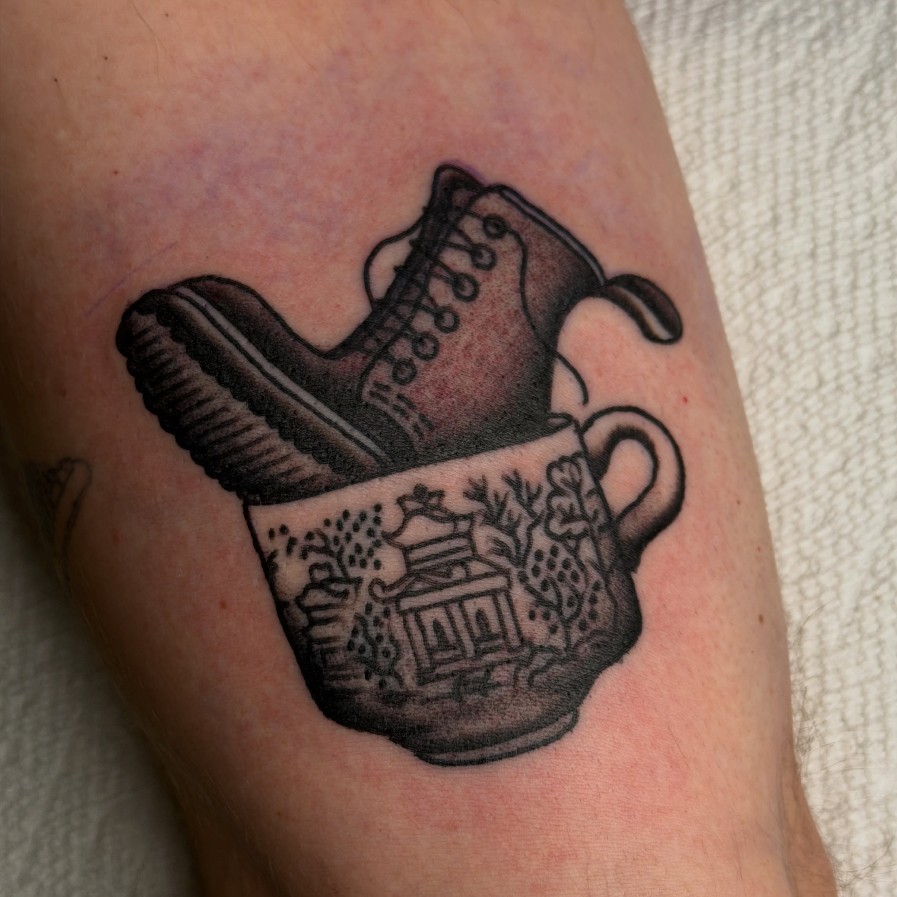 Boot in teacup black and grey tattoo on the forearm by Andrew Storm
