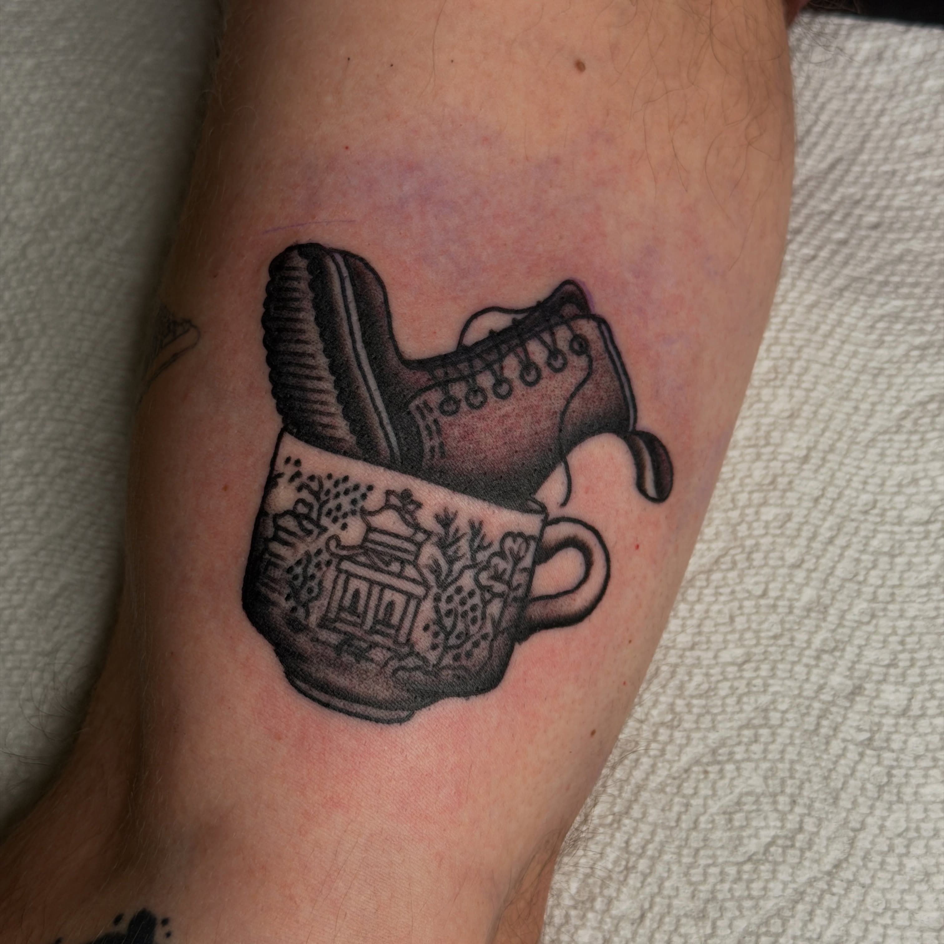 Coffee cup and shoe black and grey tattoo on the forearm by Andrew Storm