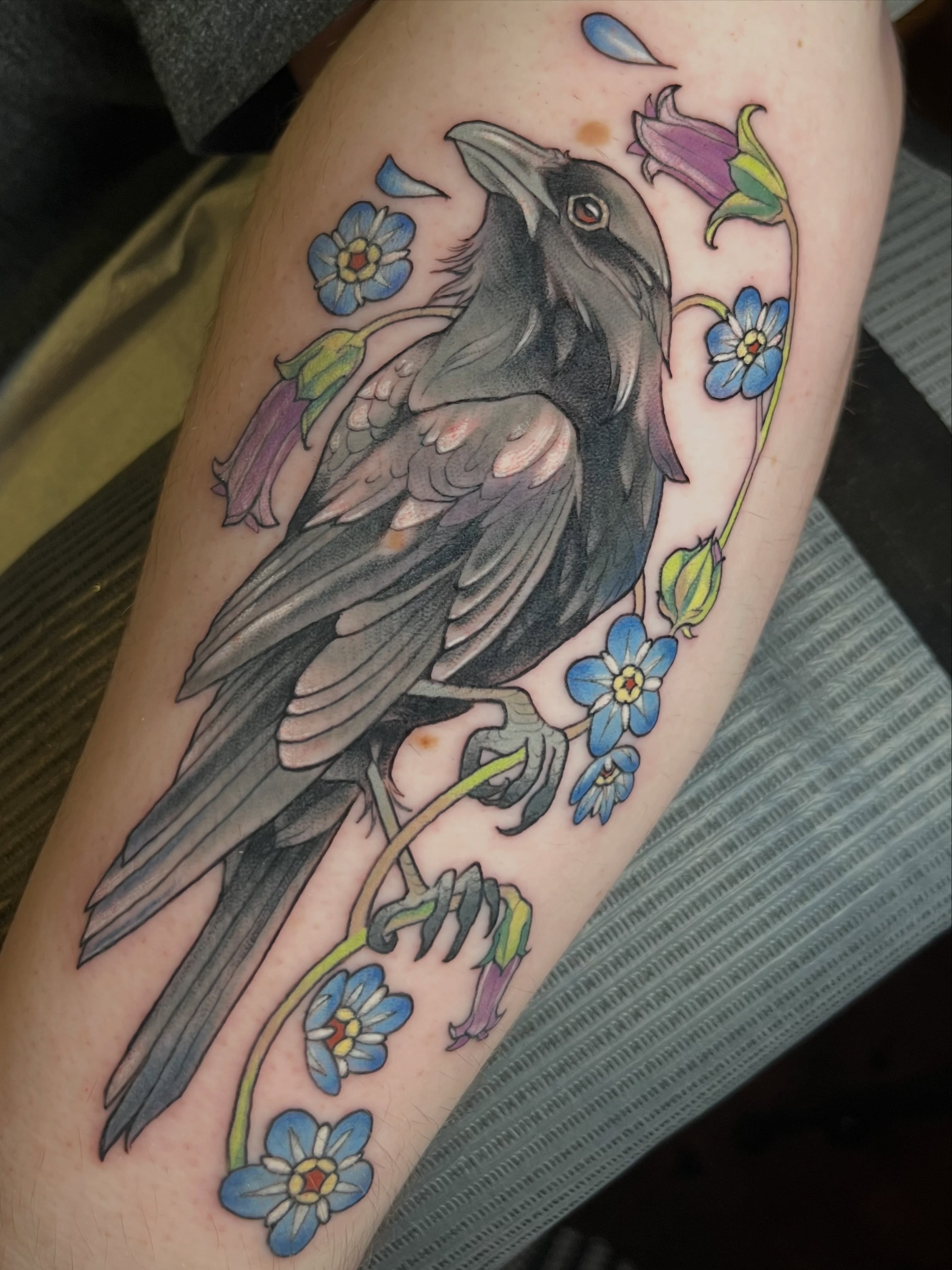 Crow and forget-me-nots realism tattoo on the forearm by Cassandra