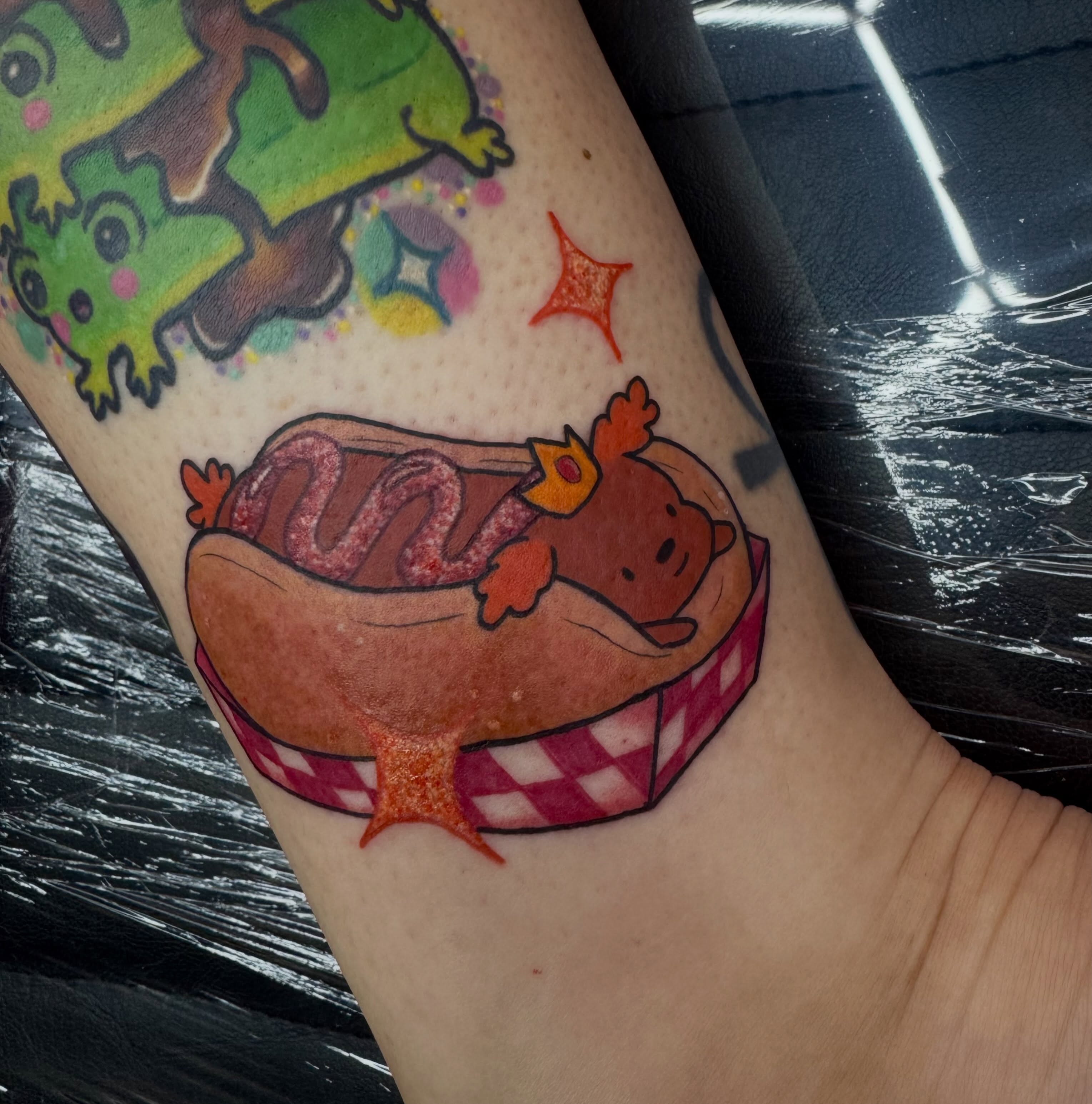 Hot dog with crown illustrative tattoo on the forearm by Jada Reynolds