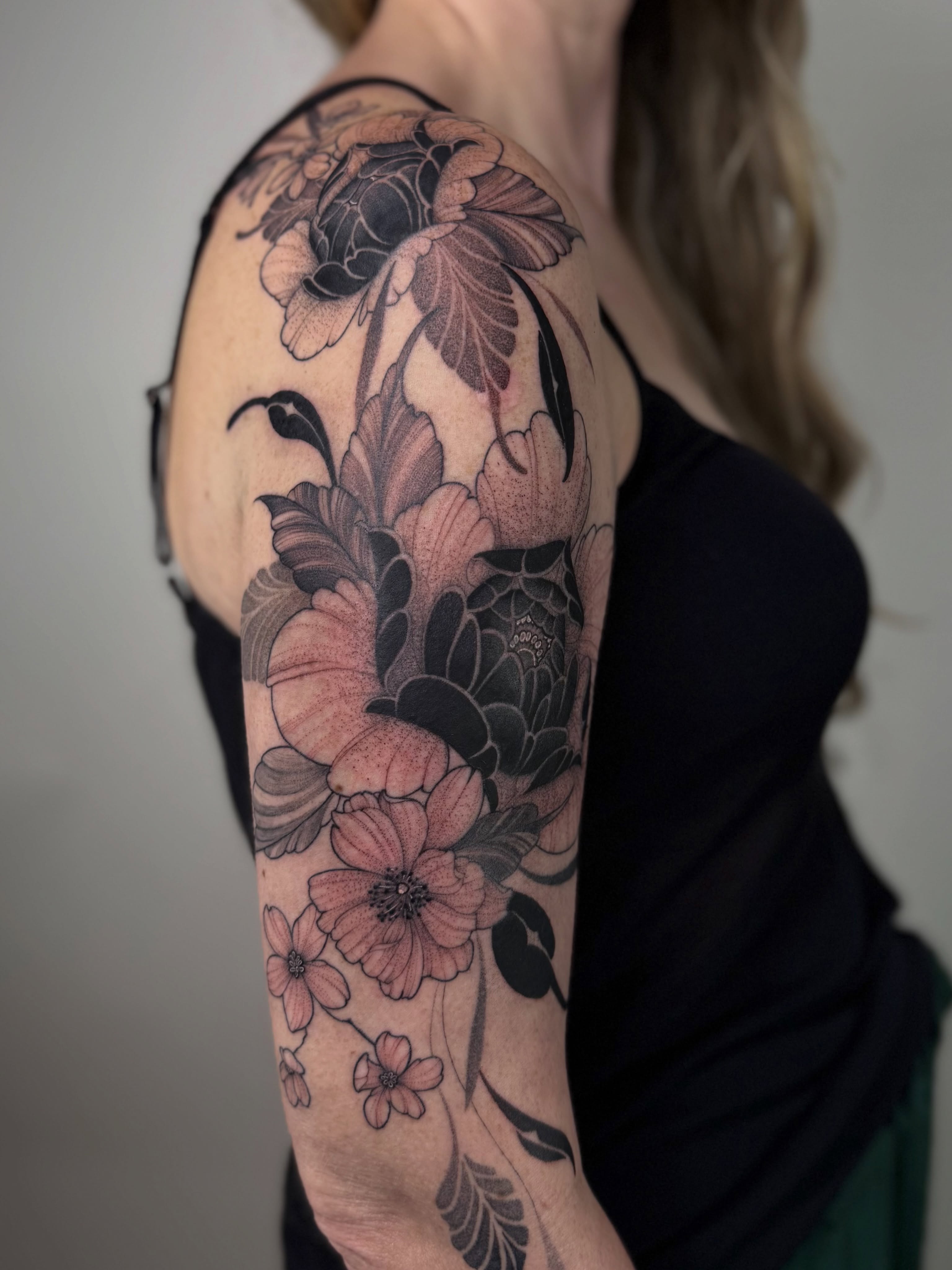 Floral arrangement black and grey tattoo on the upper arm by Jena Perry