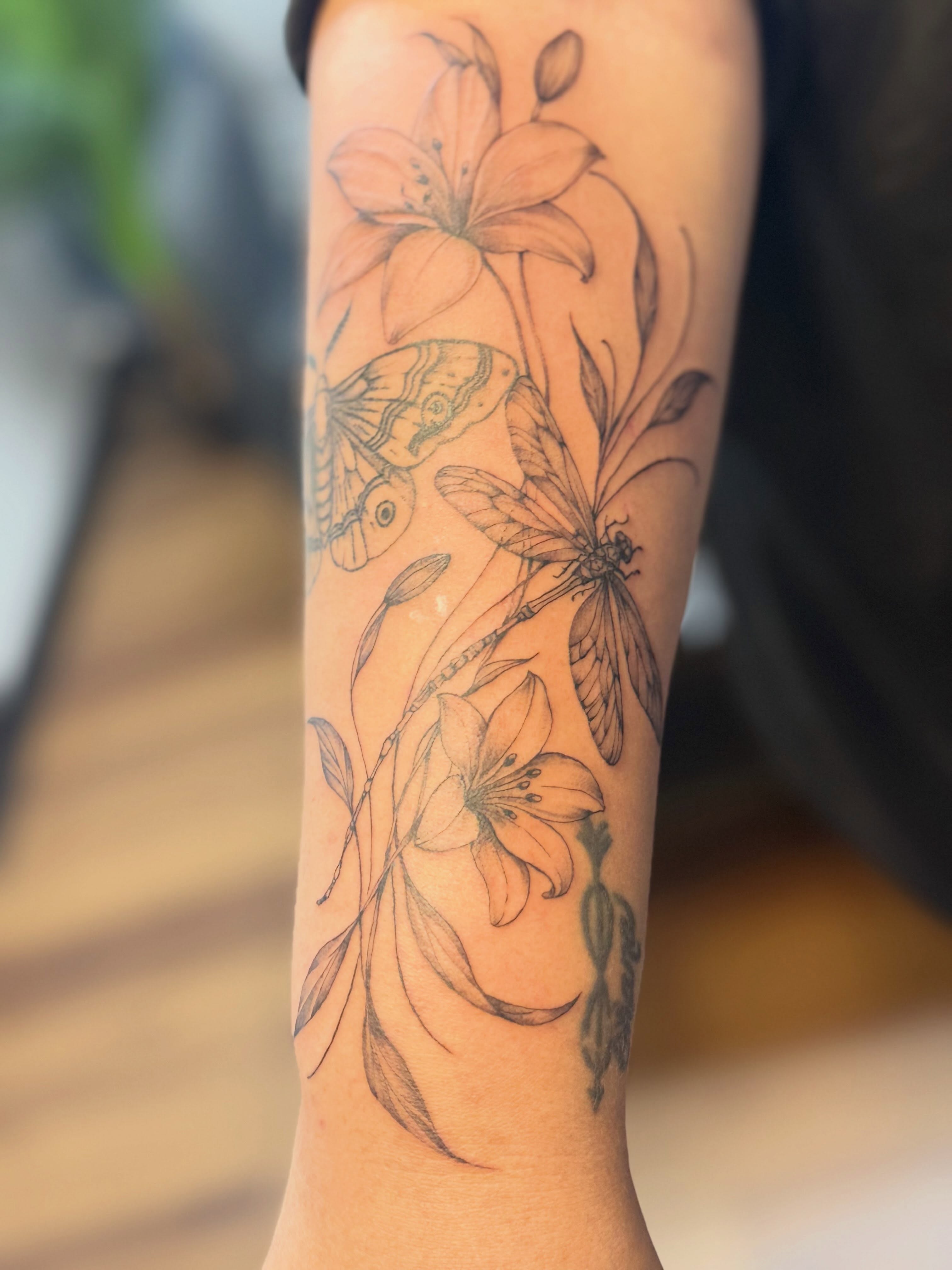 Lilies and dragonfly black and grey tattoo on the forearm by Tetiana