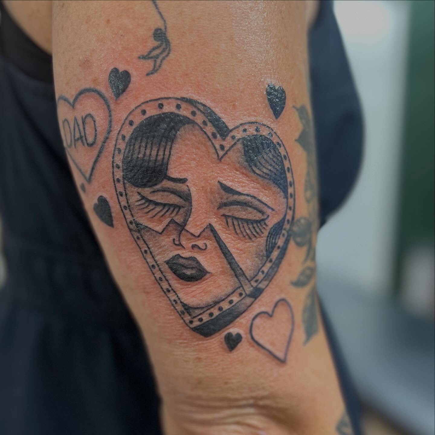 Heart with faces black and grey tattoo on the forearm by Victorian Coleman