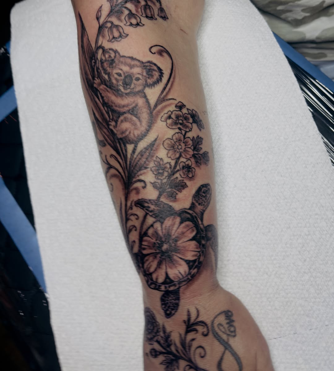 Koala and flowers black and grey tattoo on the forearm by Butz Tattoos