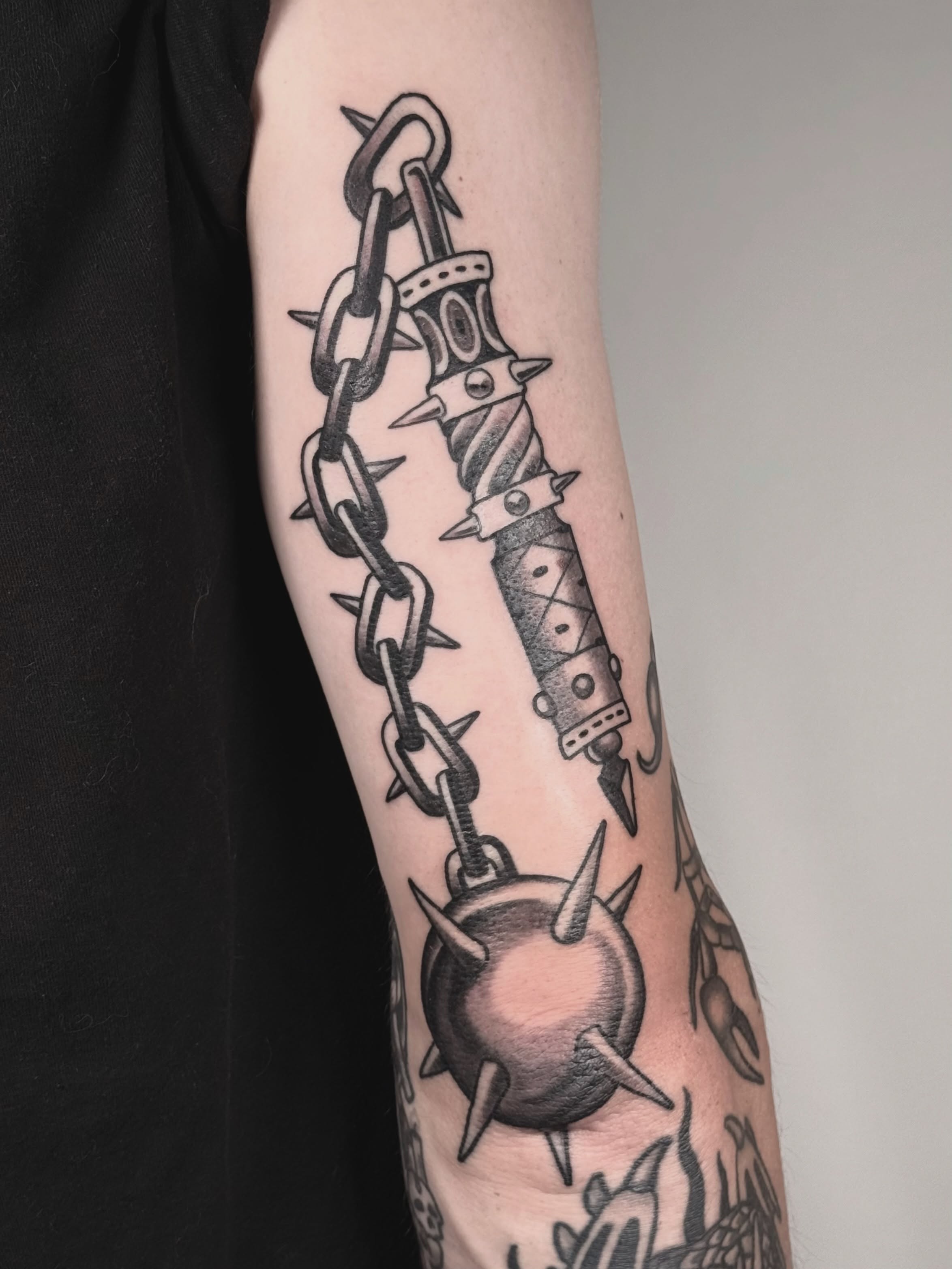 Chain and dagger black and grey tattoo on the forearm by autumn sky