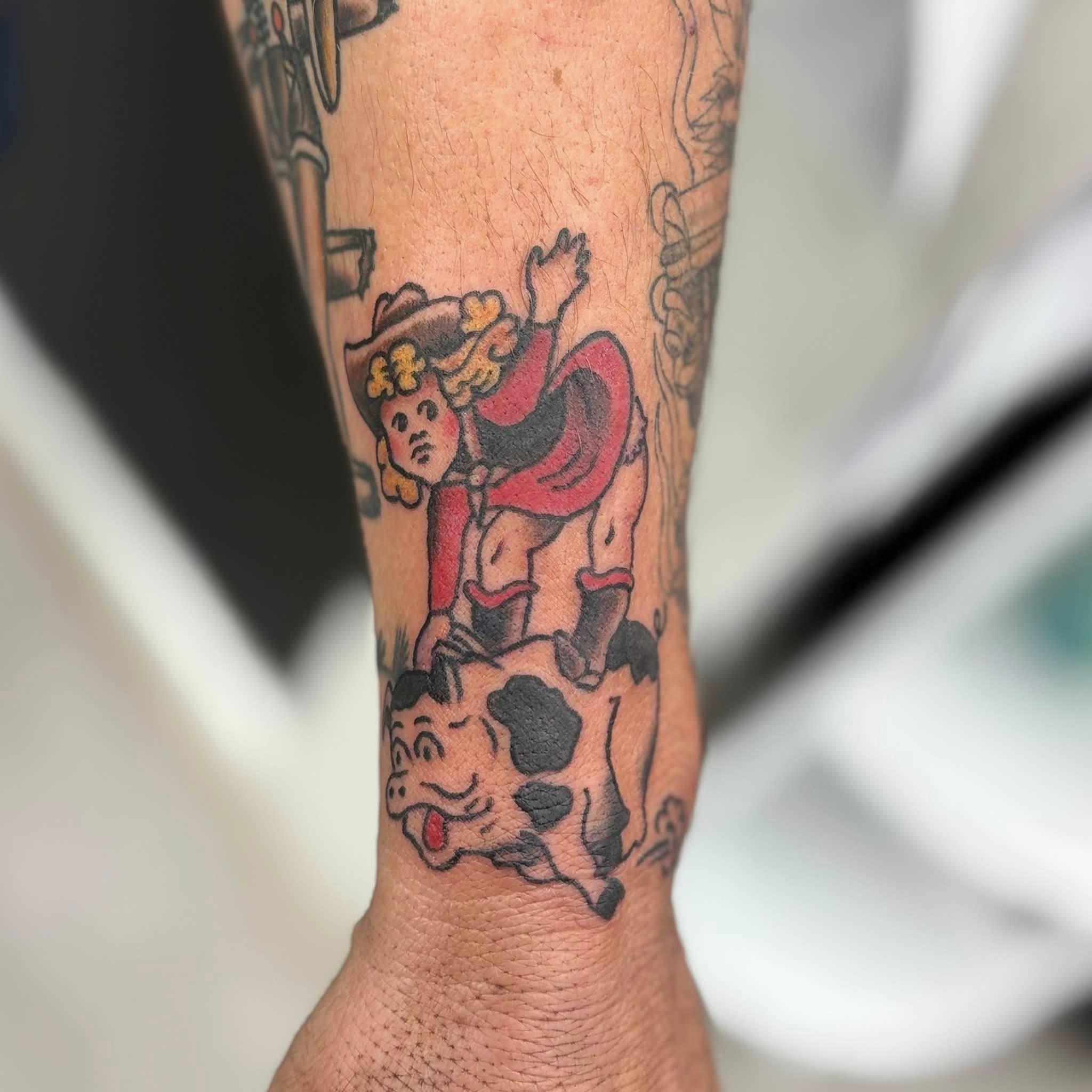 Cowgirl riding cow American traditional tattoo on the forearm by Jon Anderson