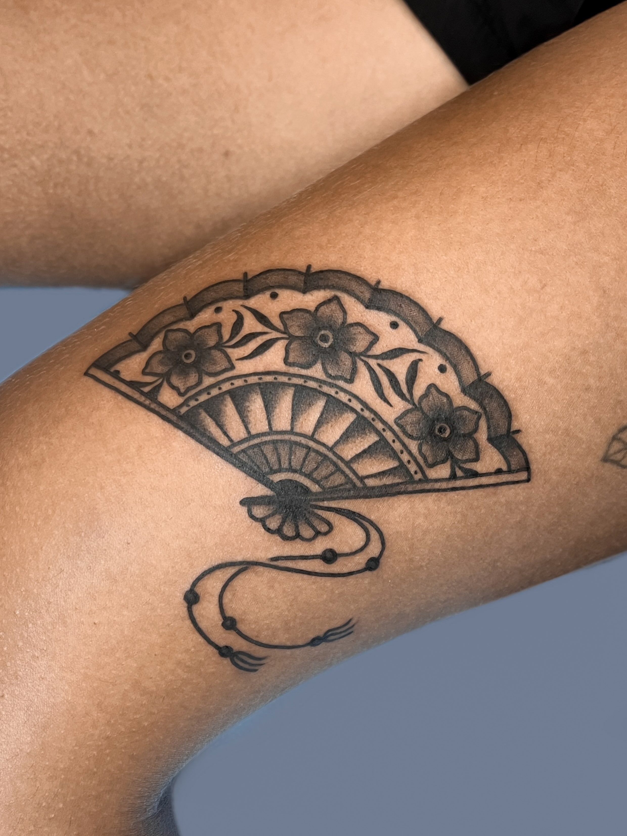 Fan with floral details black and grey tattoo on the forearm by nina
