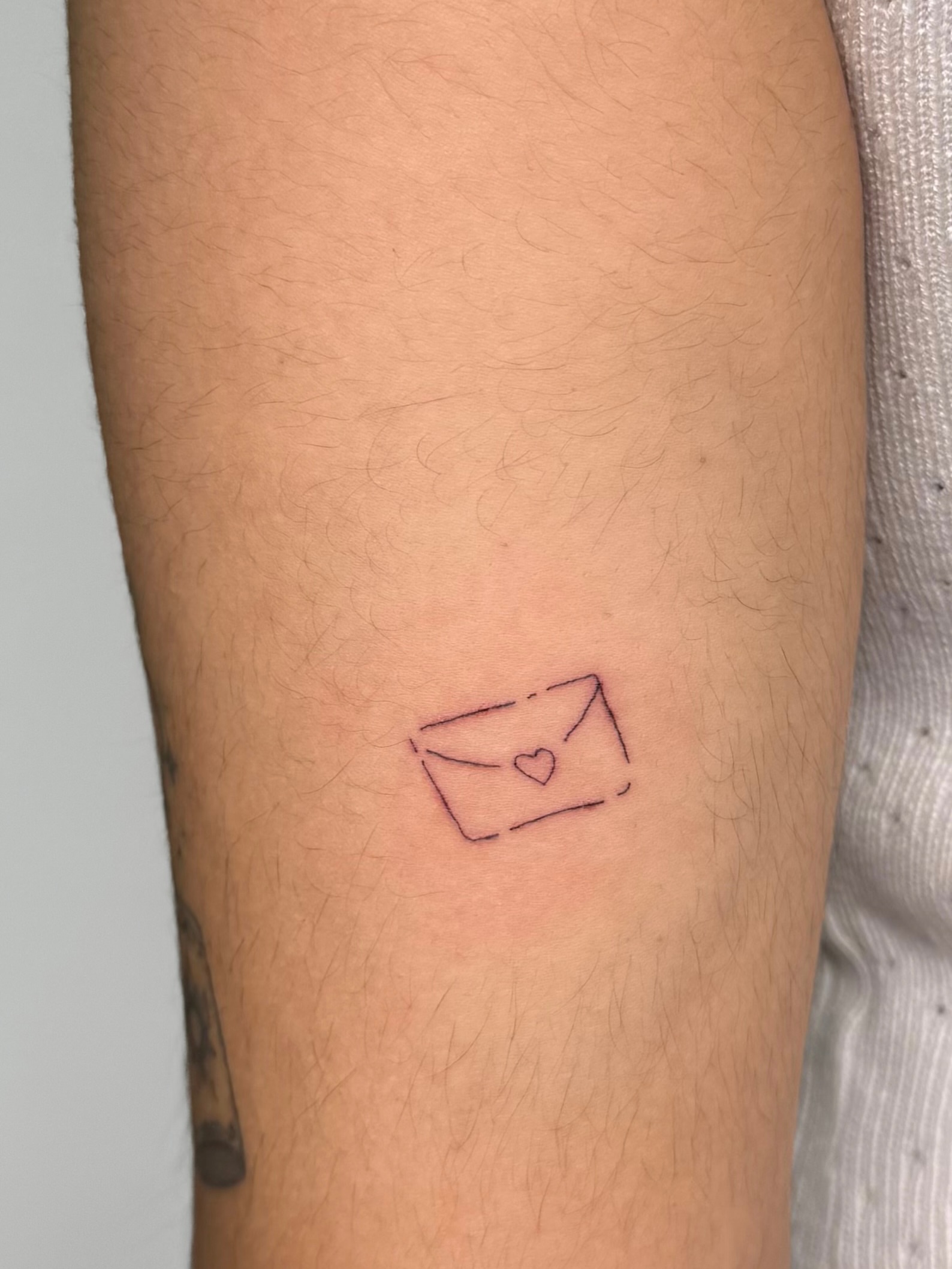 Envelope with heart minimalist tattoo on the forearm by Nicole