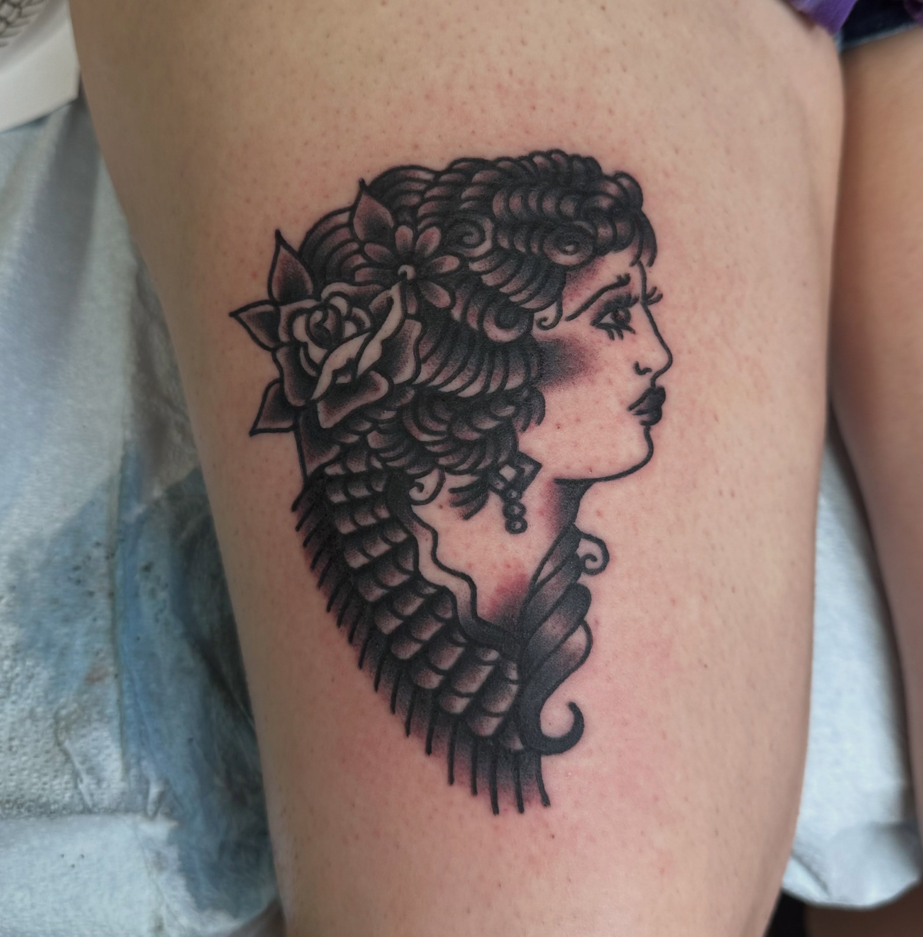 Woman with floral hair black and grey tattoo on the thigh by norawillstattoo