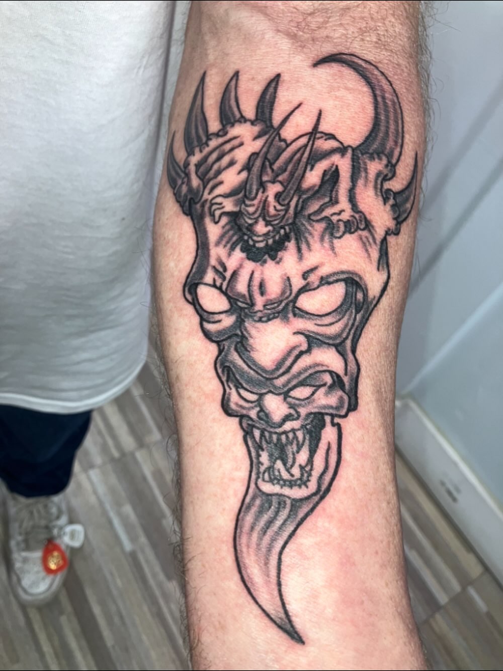 Demon mask black and grey tattoo on the forearm by Bryant Johnson
