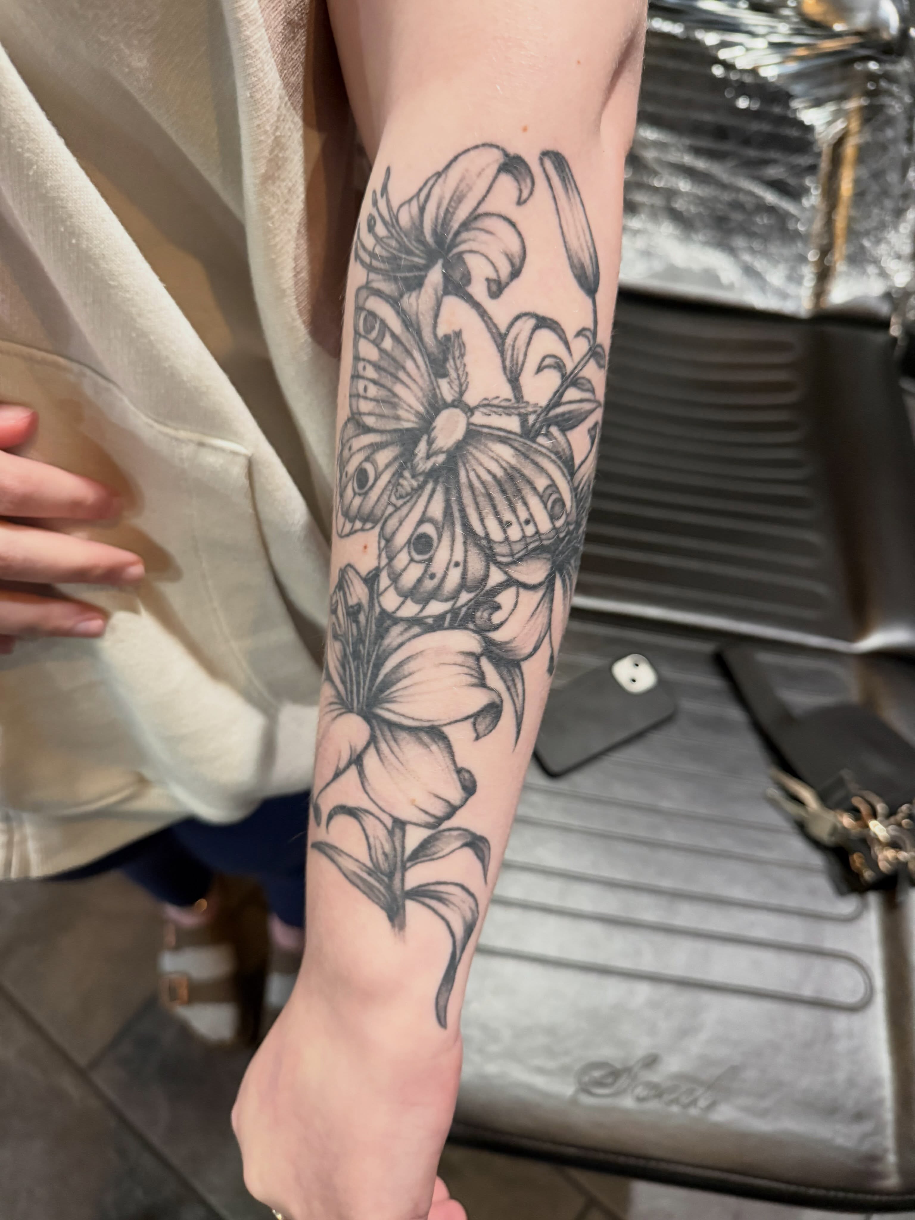 Lily and butterfly black and grey tattoo on the forearm by Courtney