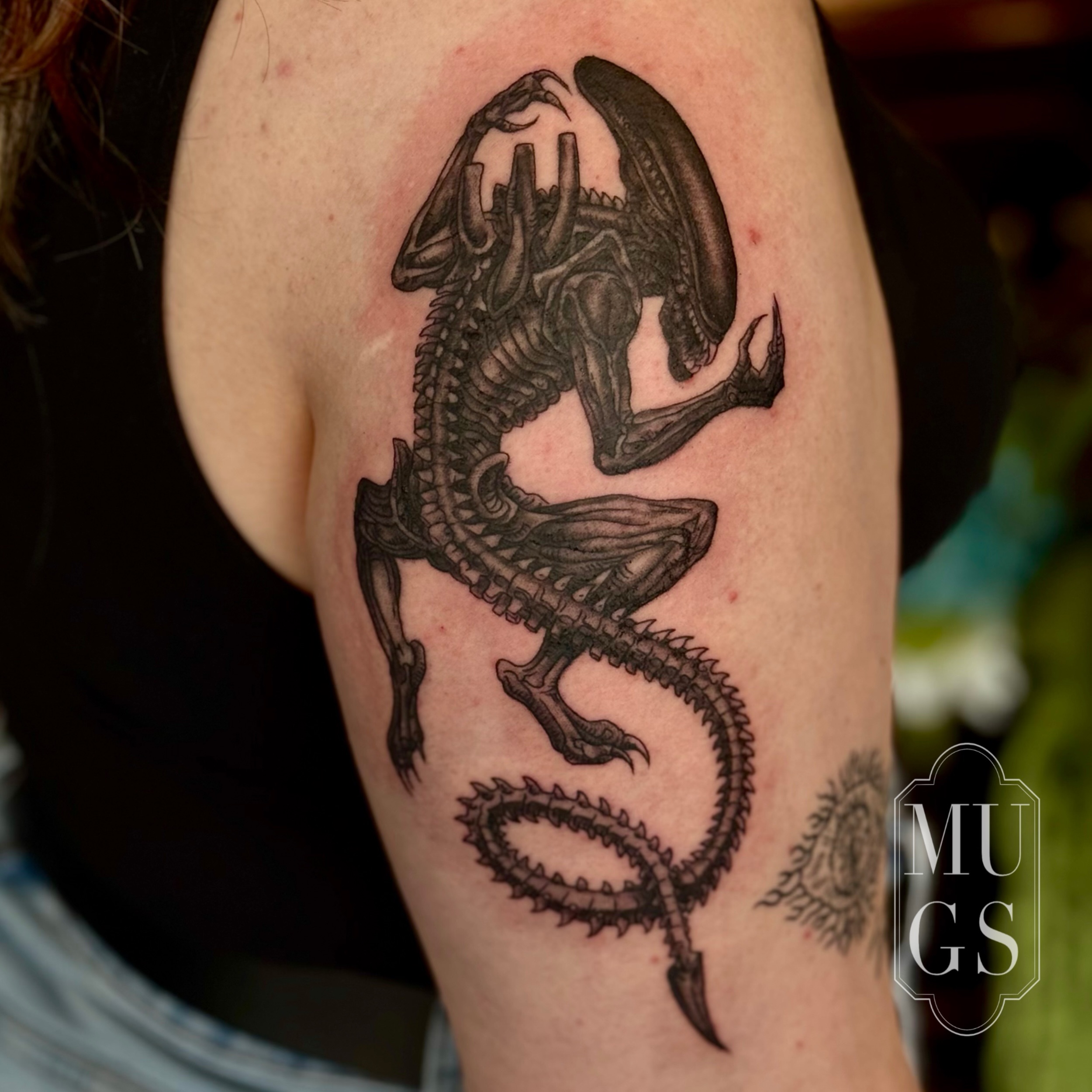 Alien creature realism tattoo on the upper arm by Emily Andreozzi